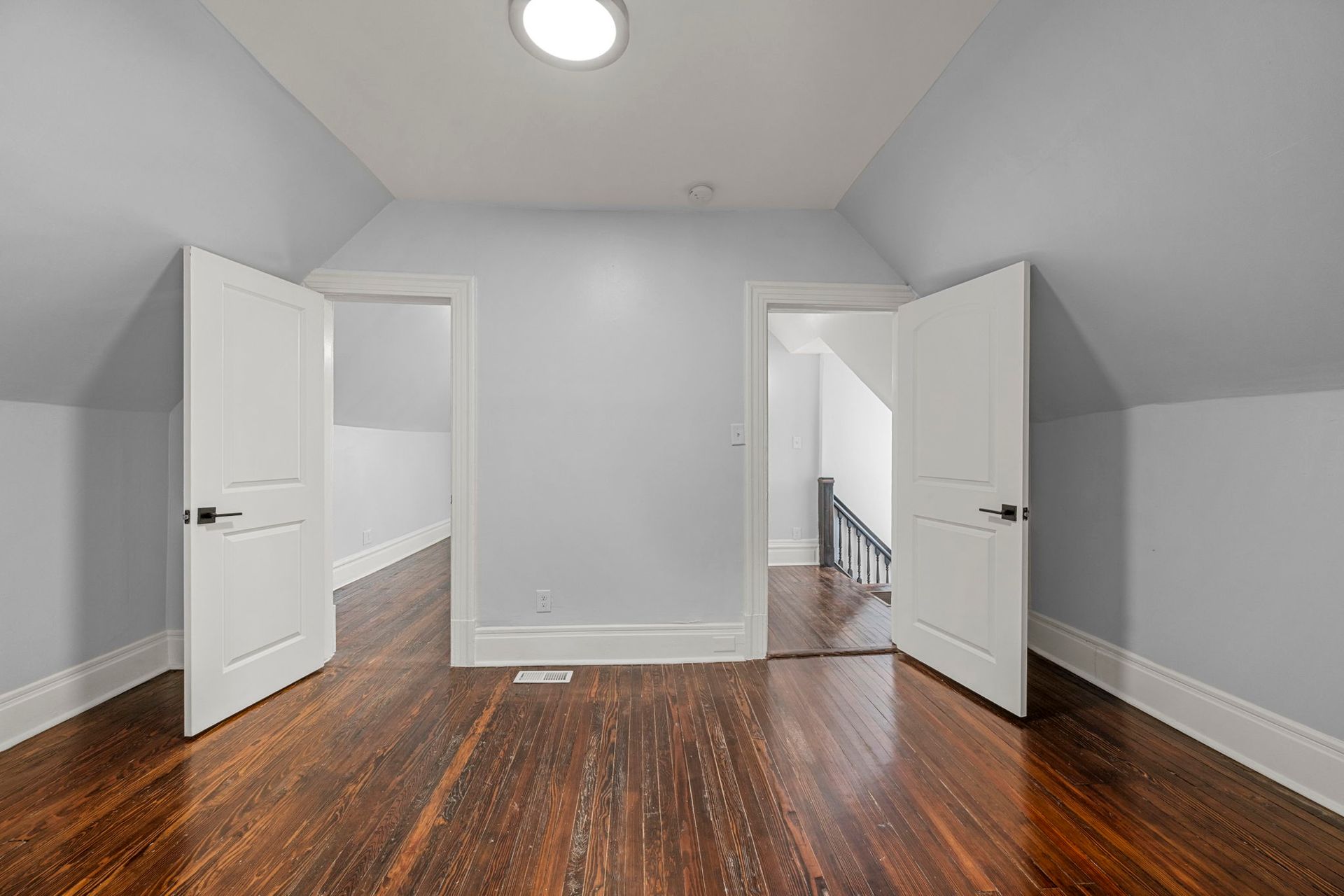 Empty room with wooden floor, two doorways, light blue walls, and white doors.