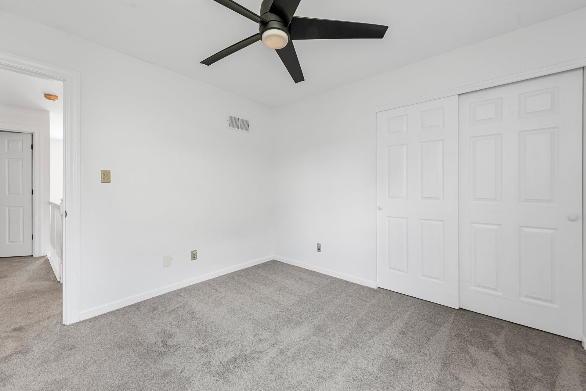 An empty bedroom with a ceiling fan and a gray carpet.