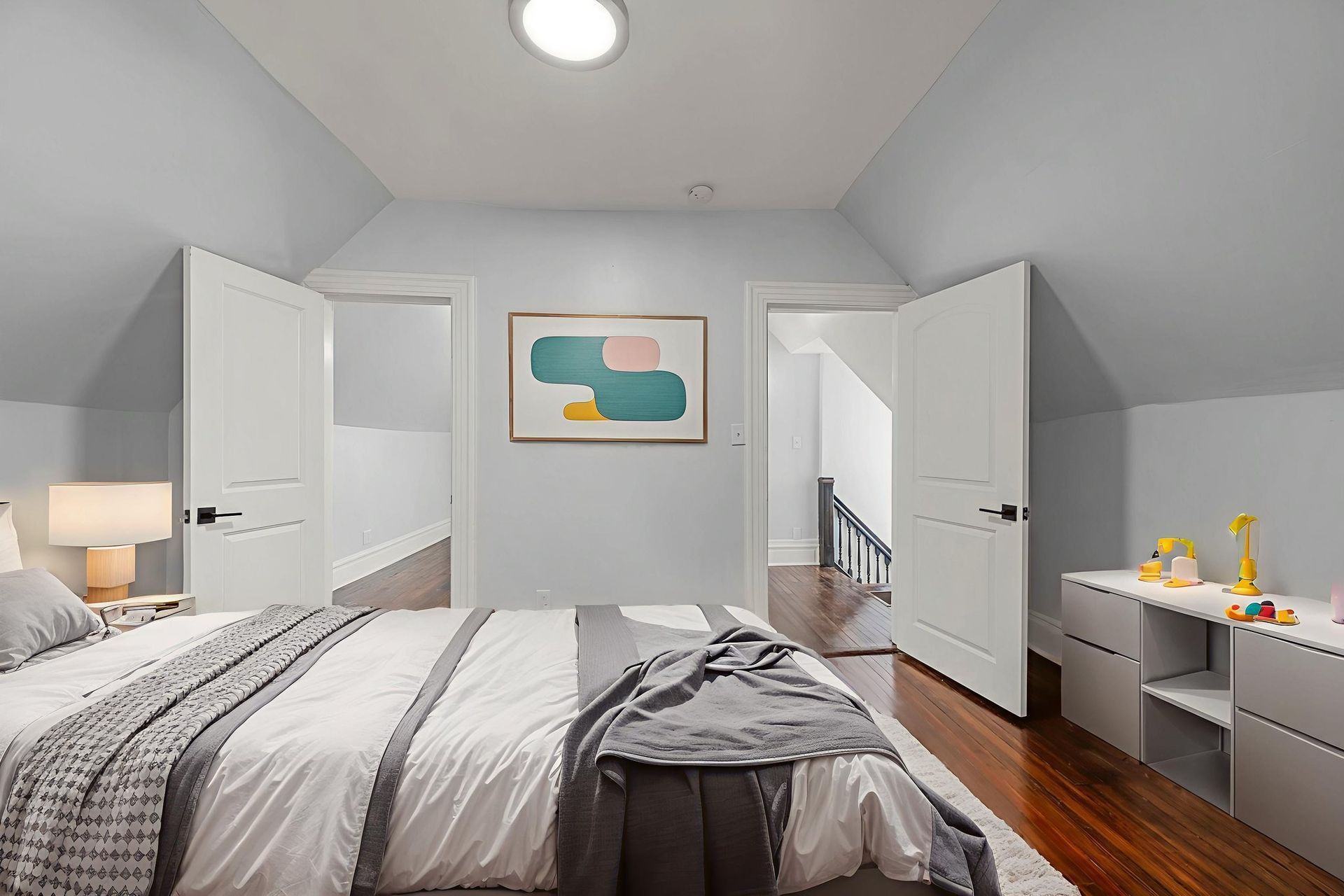 Bedroom with bed, artwork, and open doors to other rooms; light blue walls.