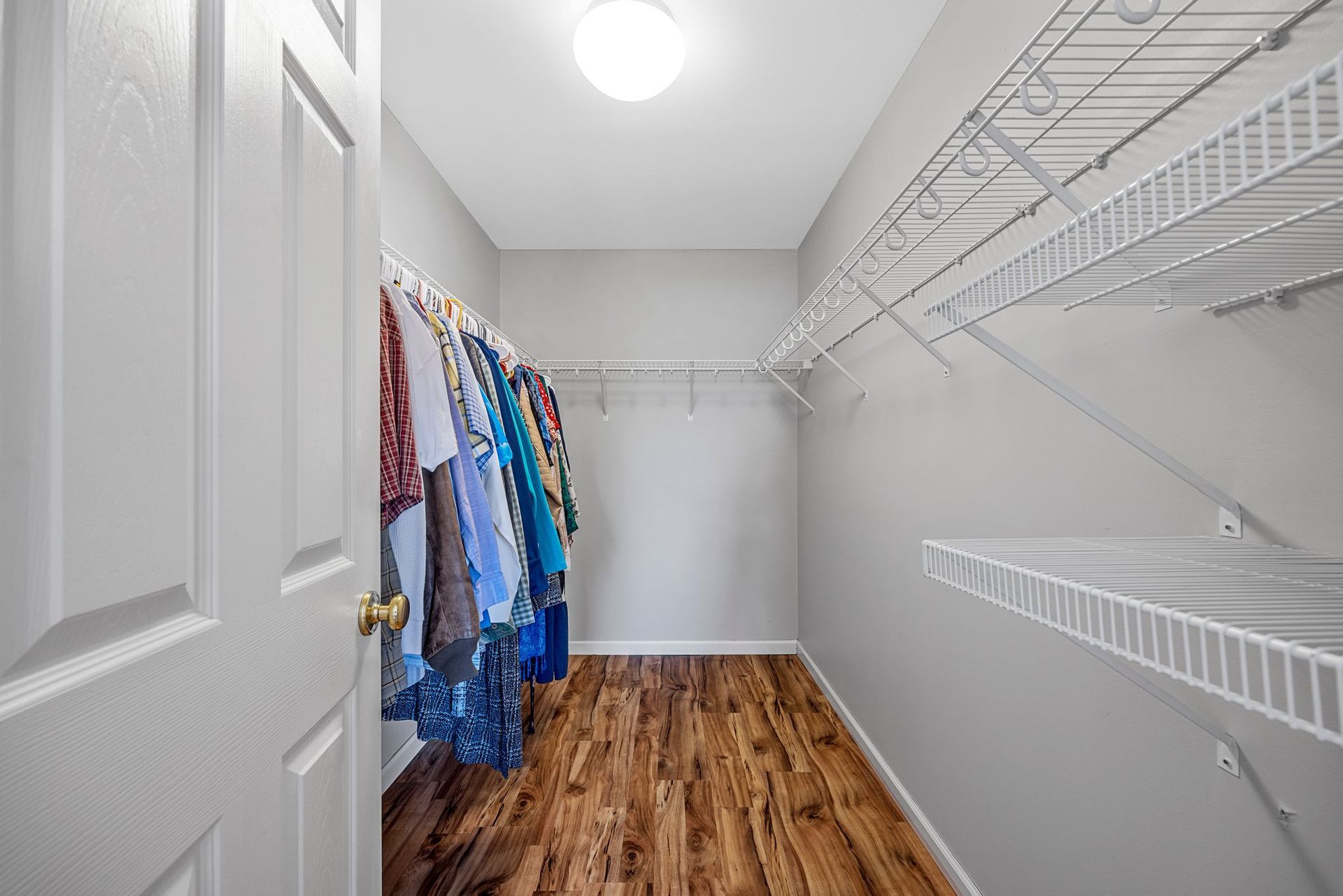 A walk in closet with clothes hanging on the wall and shelves.