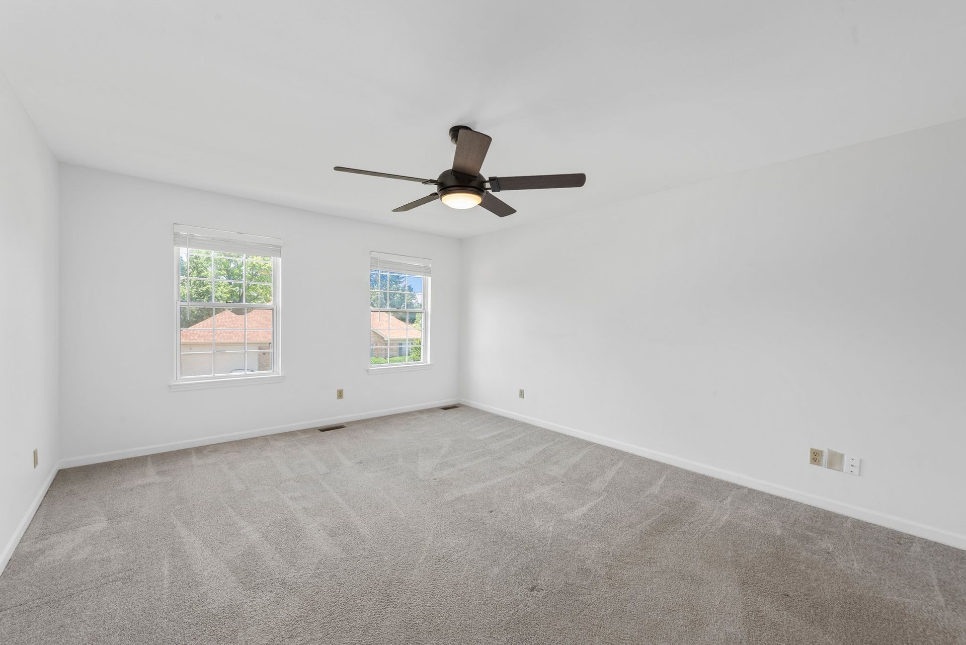 An empty bedroom with a ceiling fan and two windows.
