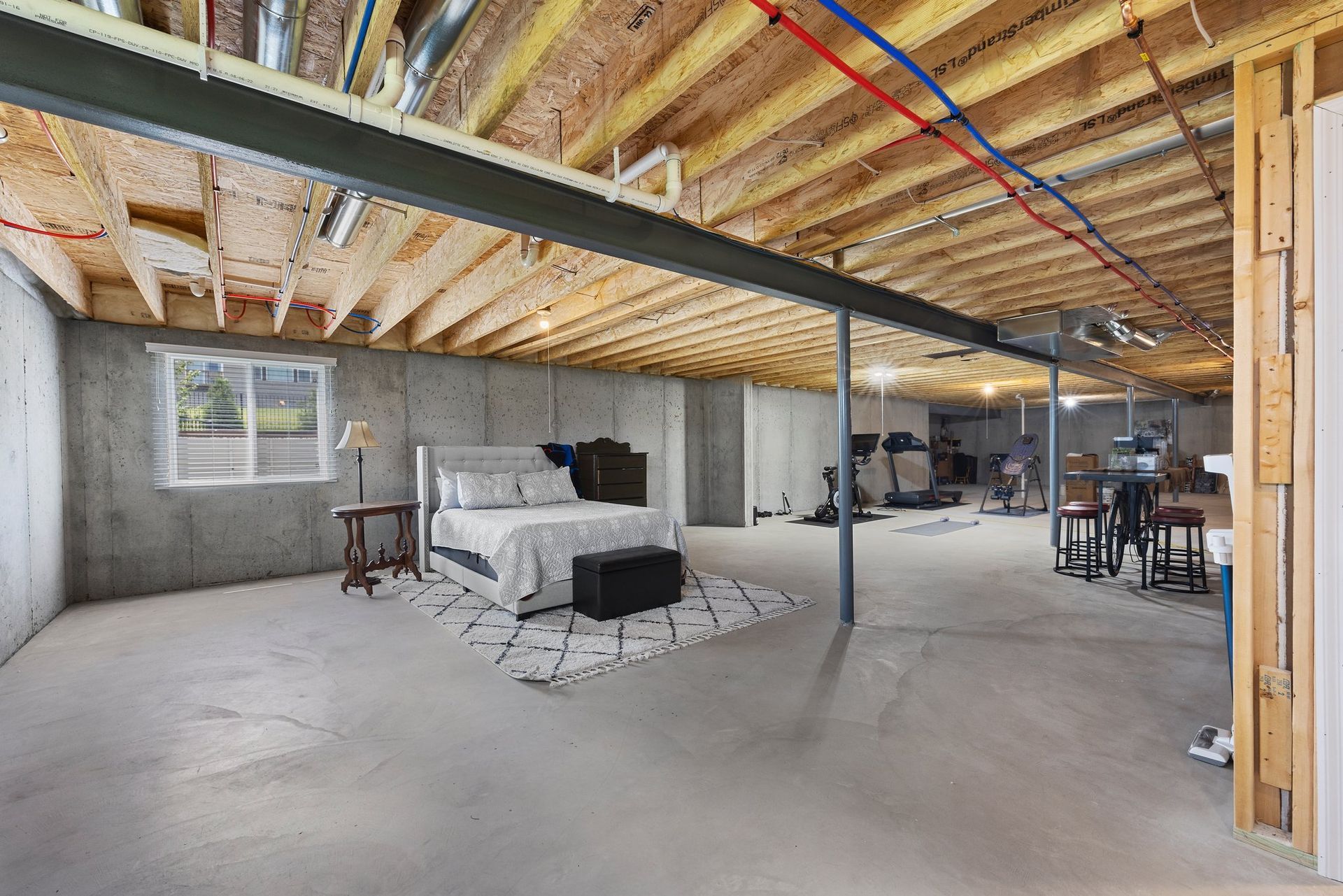 A bedroom in a basement with a bed and a window.