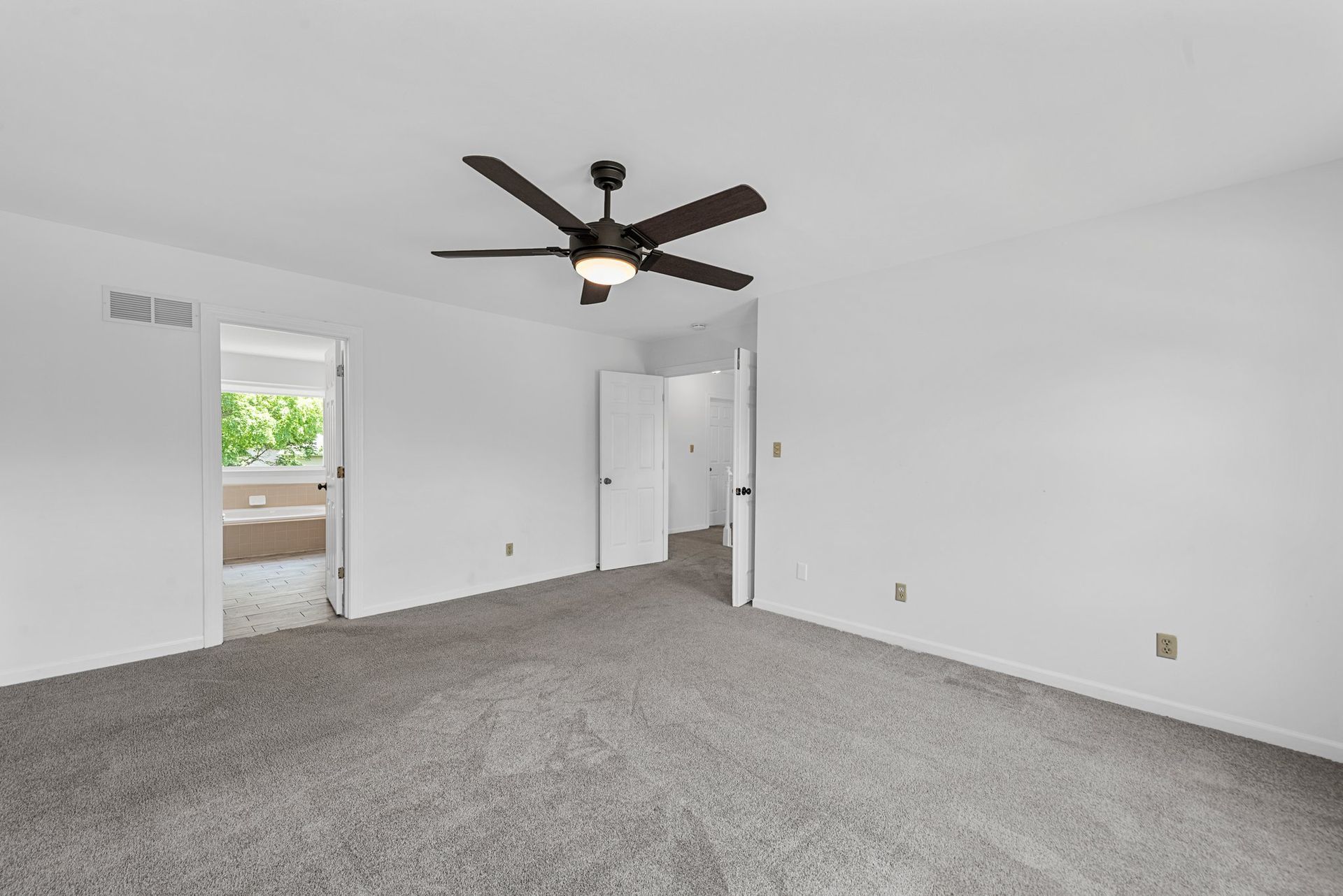 An empty bedroom with a ceiling fan and a gray carpet.