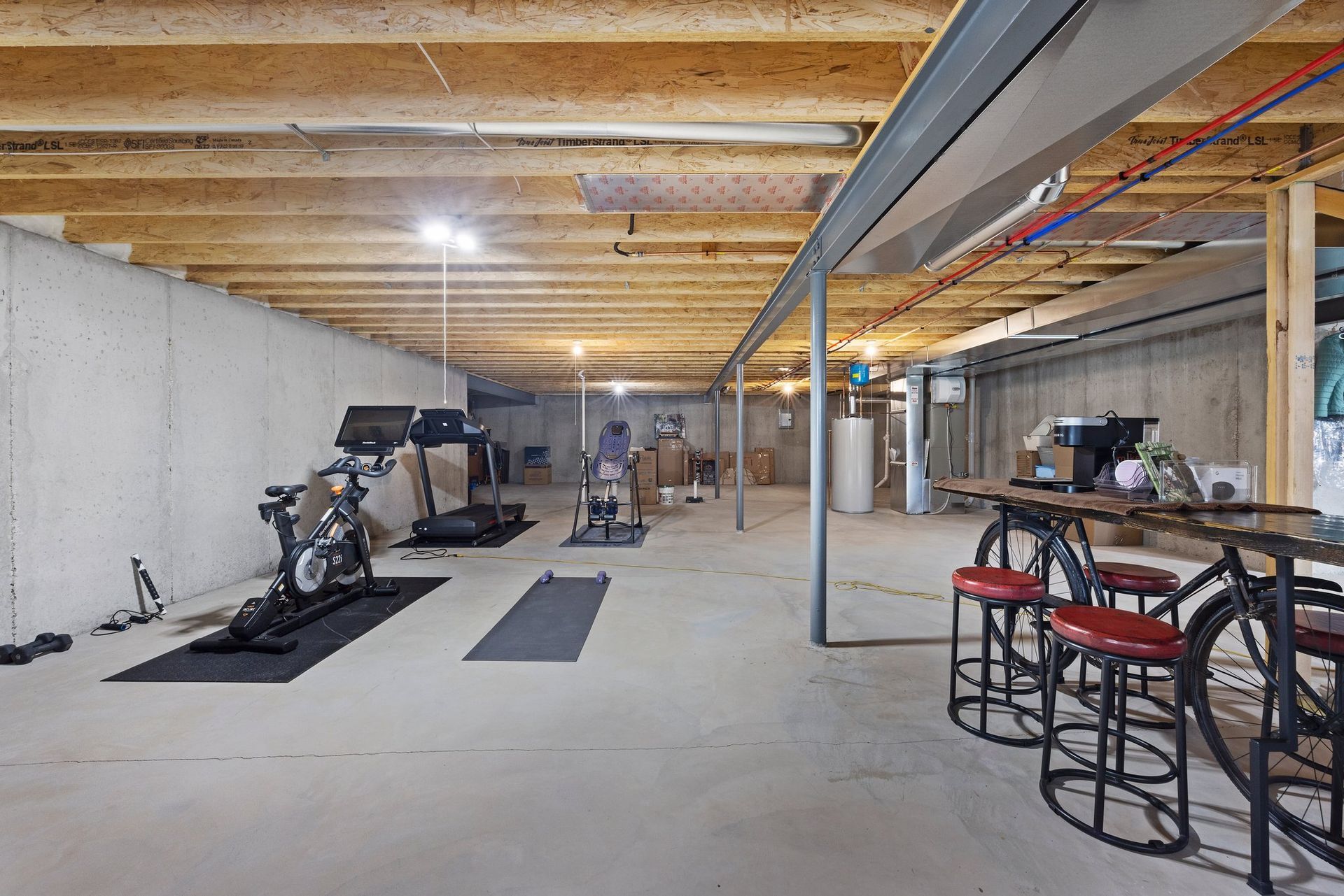 A basement with a treadmill , bikes , and a table.