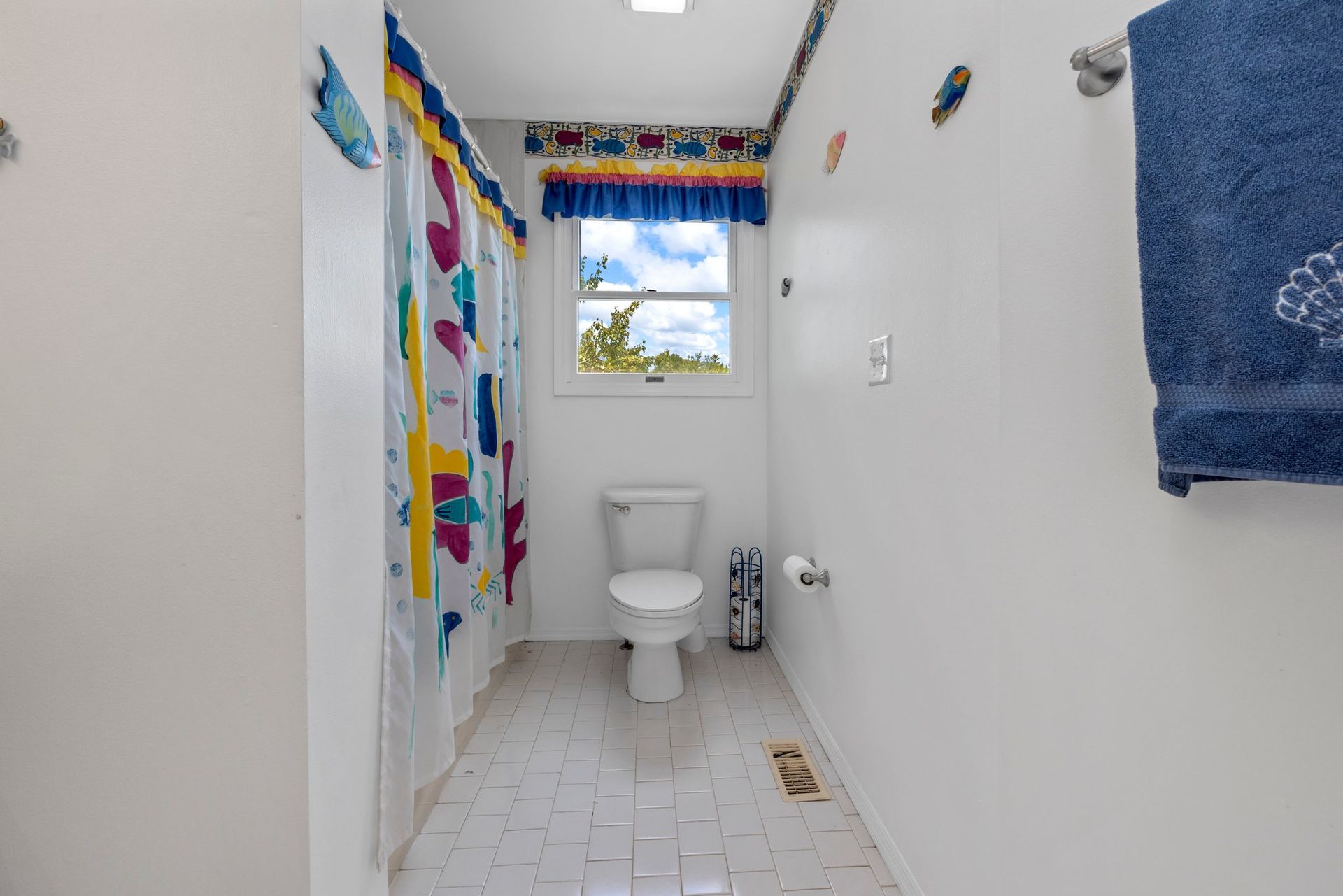 A bathroom with a toilet , shower curtain , and blue towels.