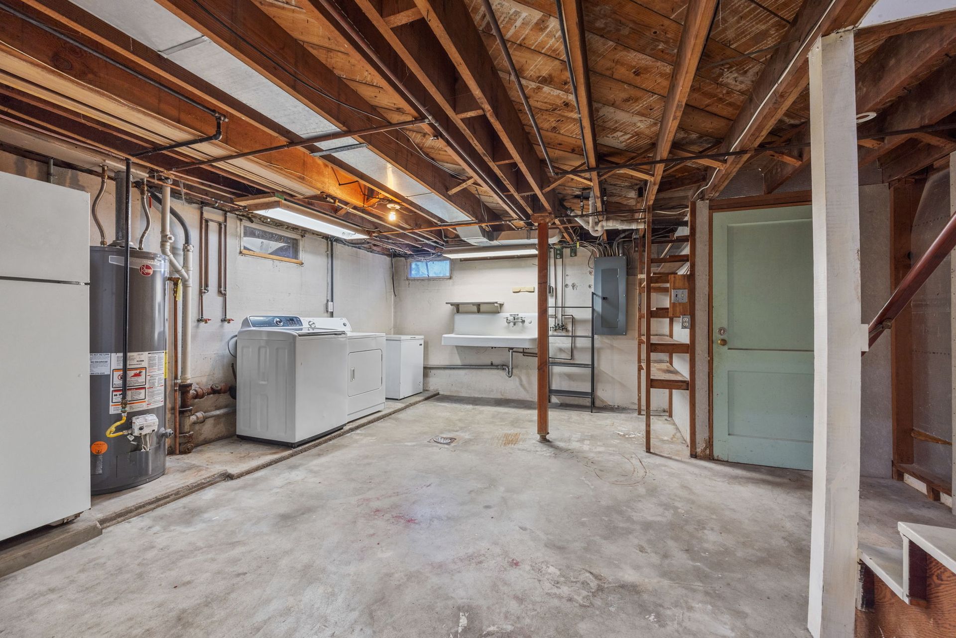 An empty basement with a refrigerator , washer and dryer , and stairs.