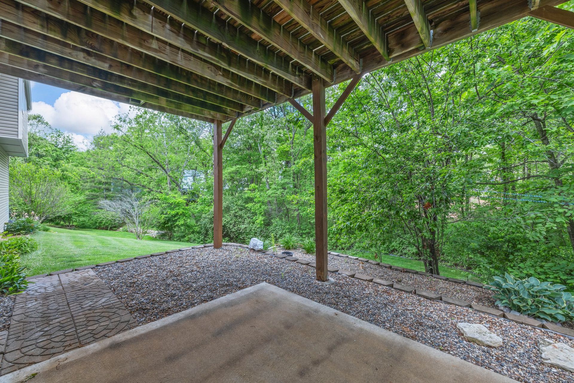 A covered patio with a wooden deck and trees in the background.