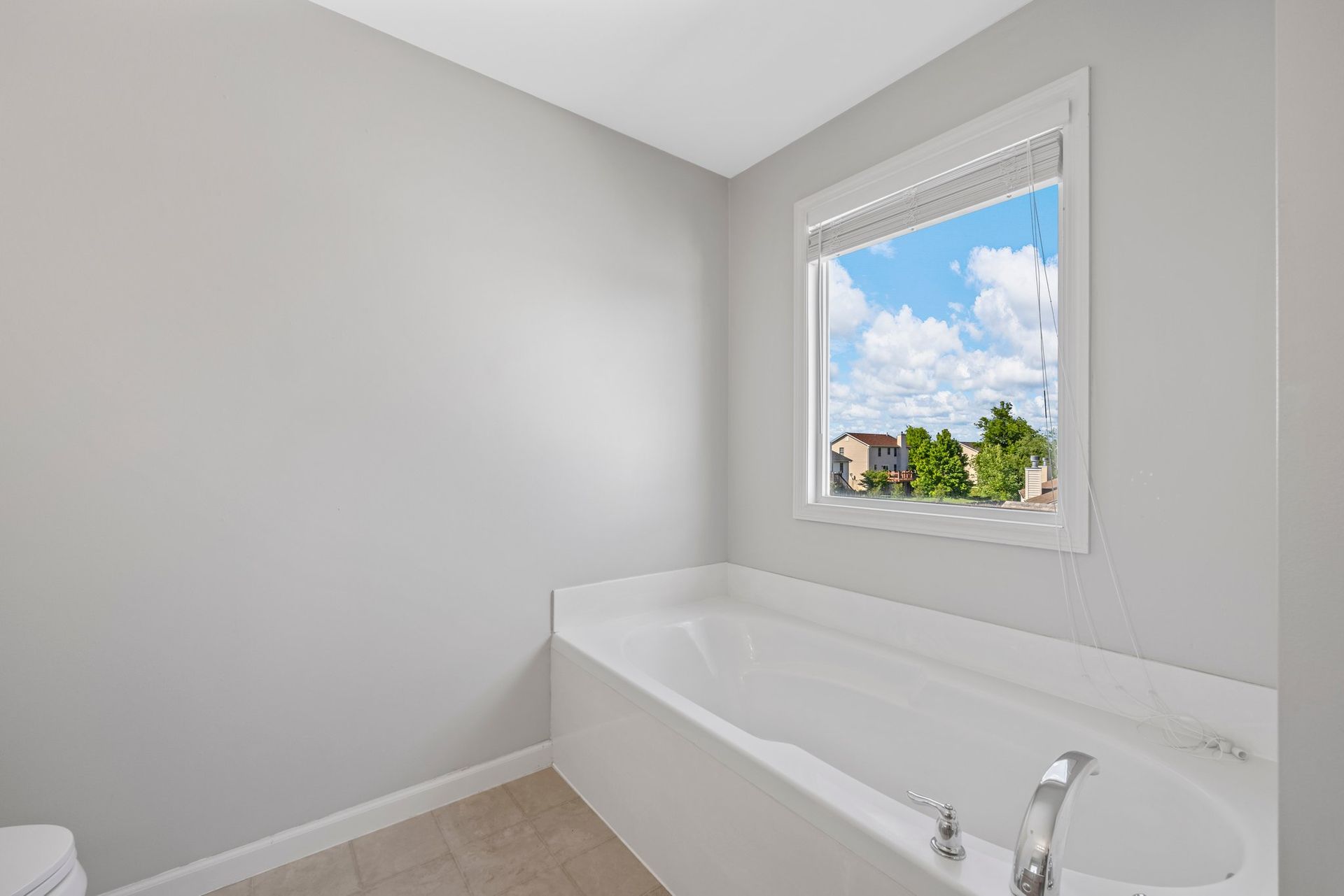 A bathroom with a tub , toilet , and window.