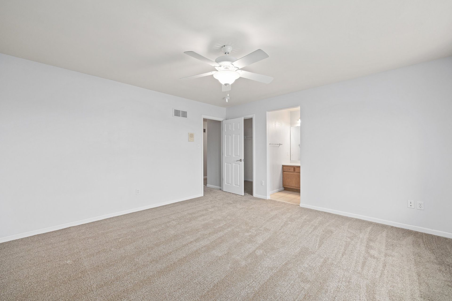 An empty bedroom with a ceiling fan and a carpeted floor.