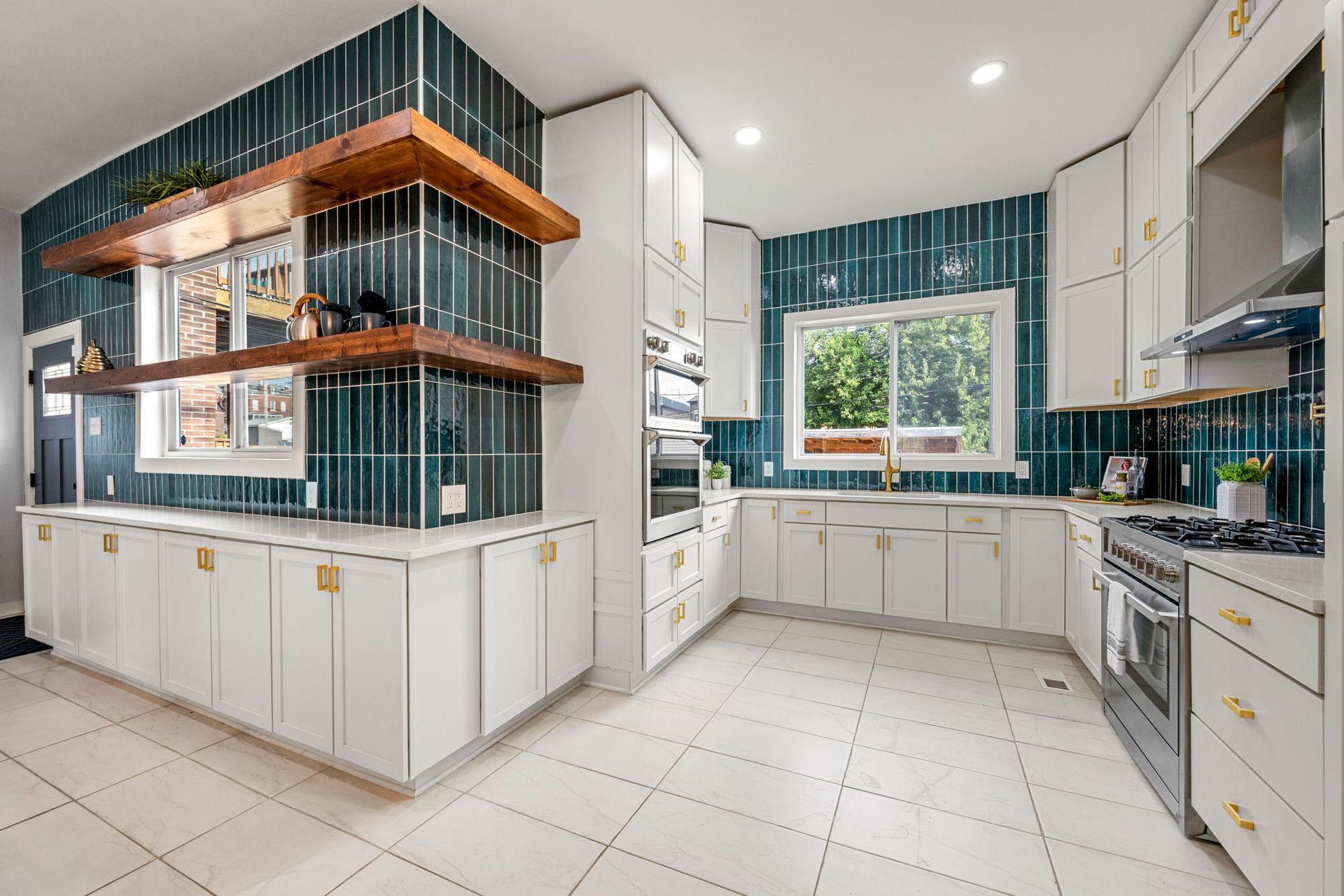 Bright kitchen with white cabinets, teal tile, wooden shelves, and a window.