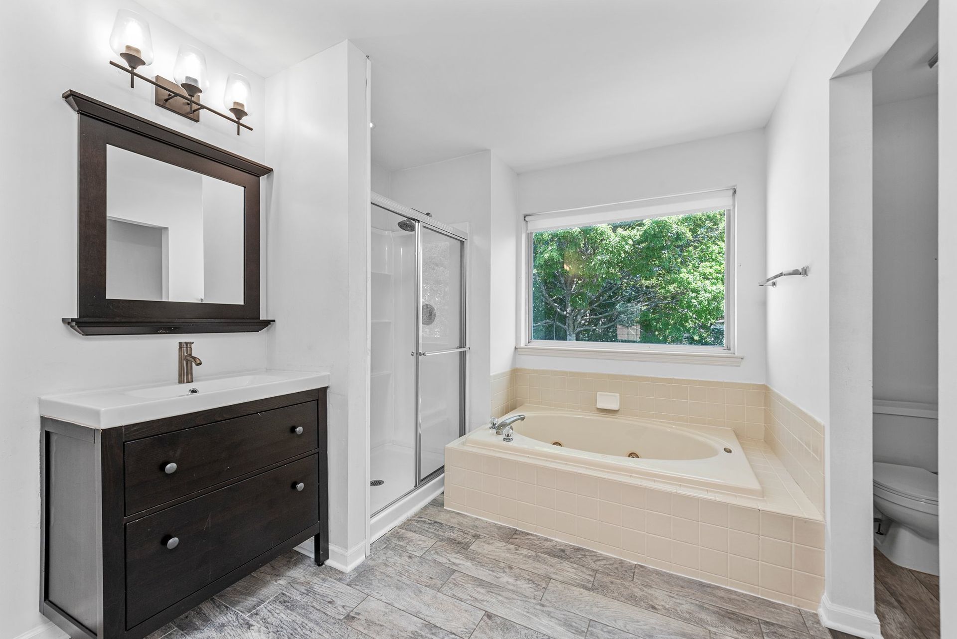A bathroom with a tub , sink , mirror and window.