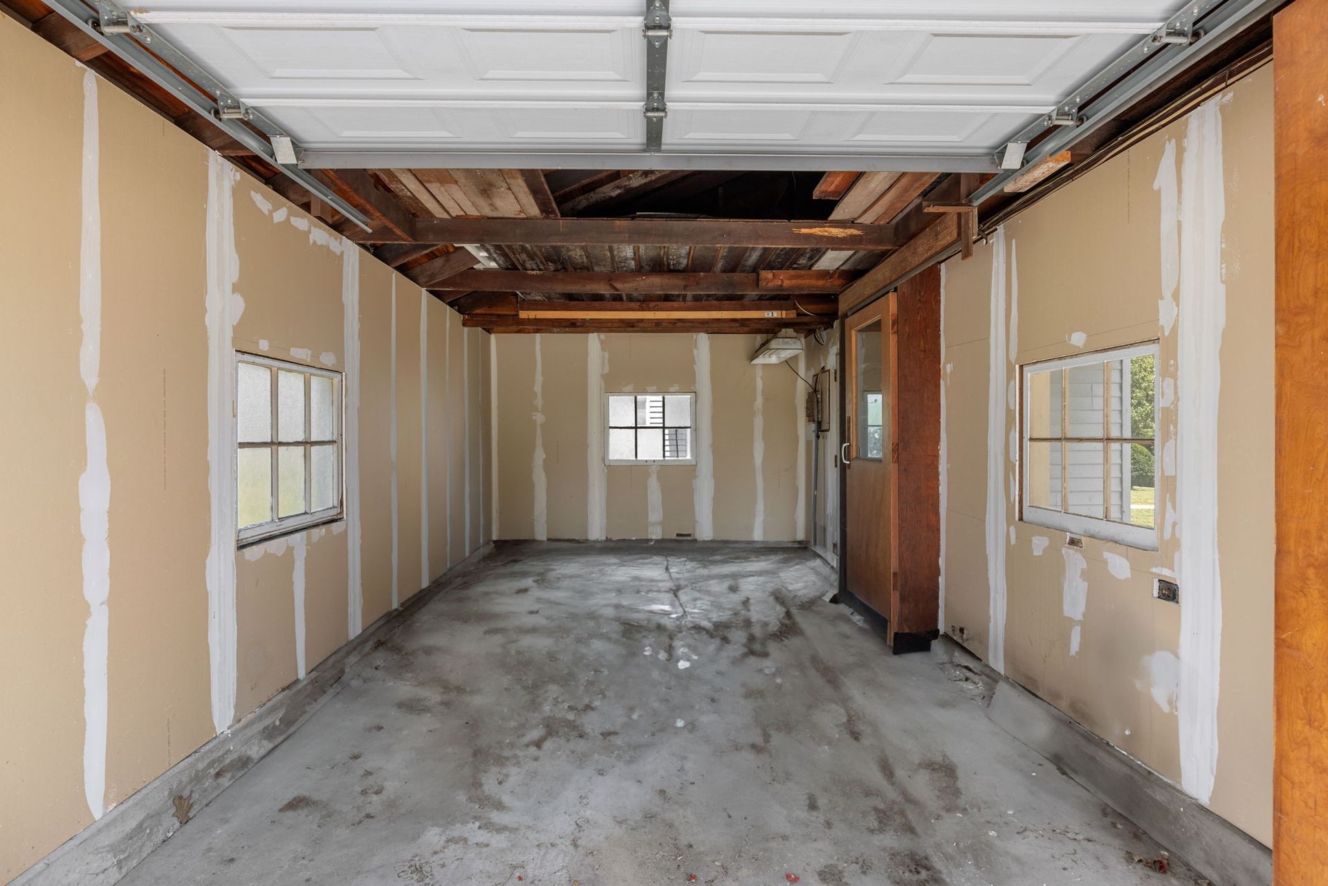 An empty garage with a garage door open and windows.