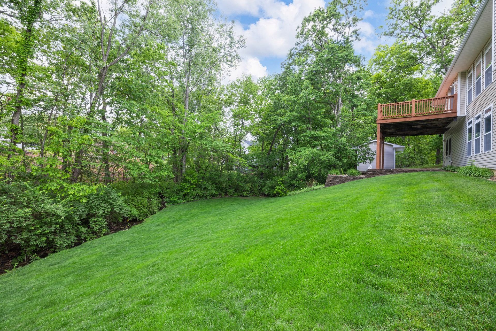 A large lush green lawn in front of a house with a deck.