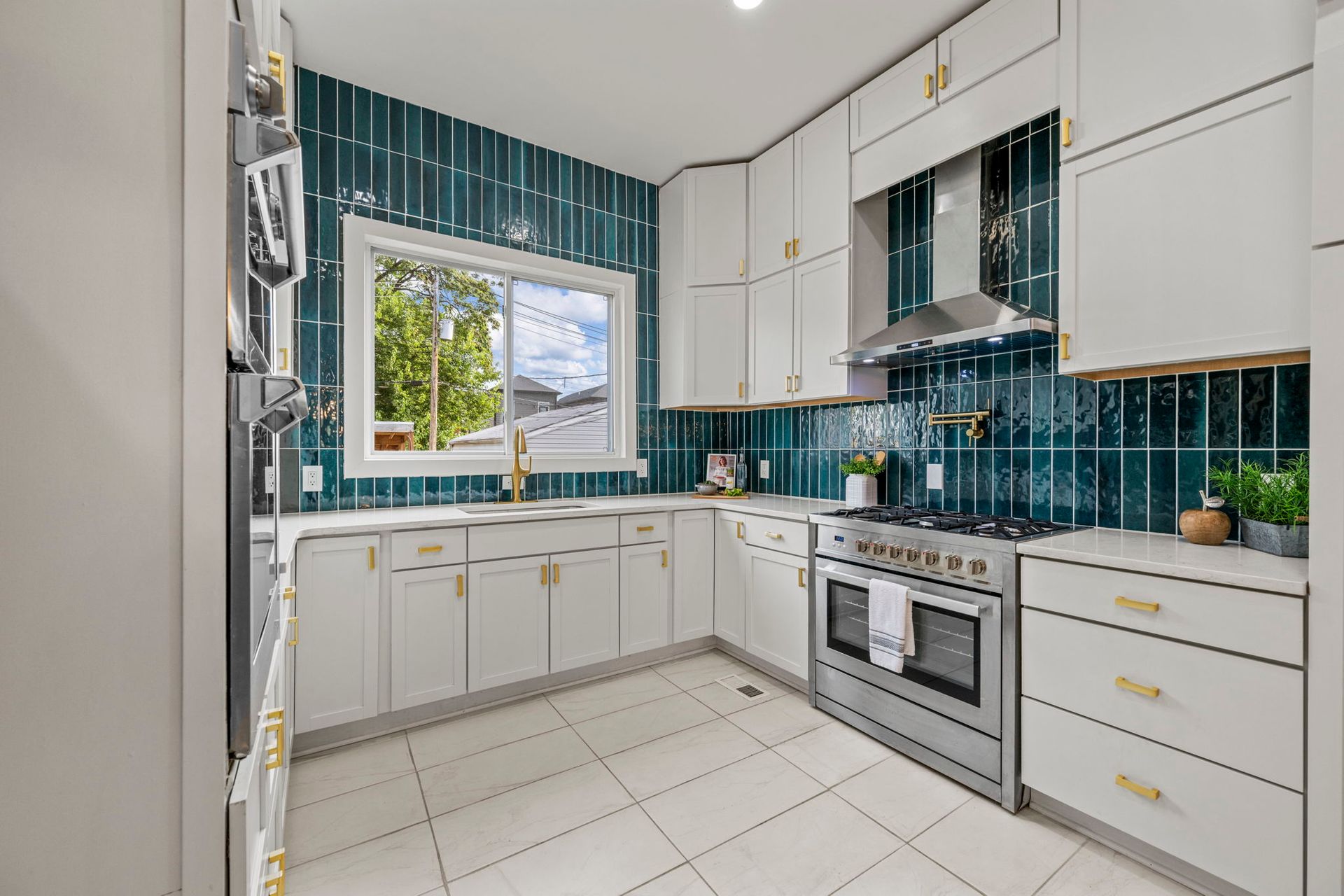 White kitchen with teal backsplash, stainless steel appliances, and gold hardware.