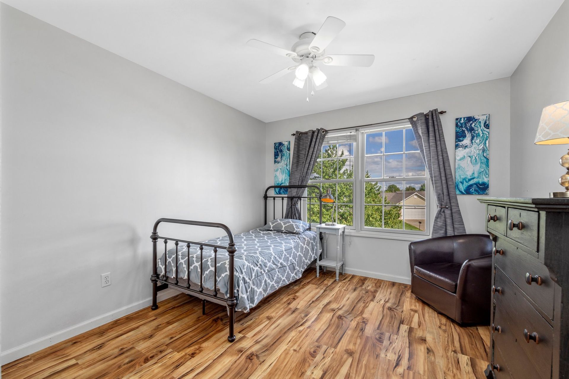 A bedroom with a single bed , chair , dresser and ceiling fan.