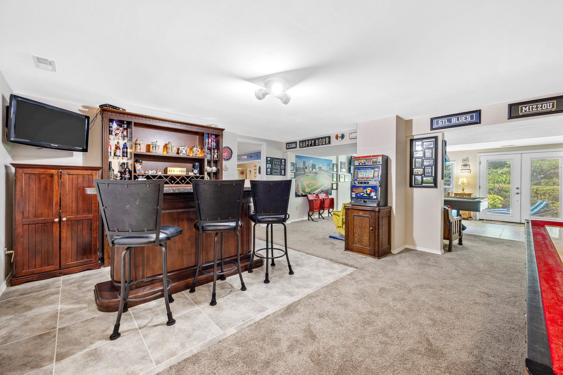 A basement with a bar , stools , a pool table and a television.