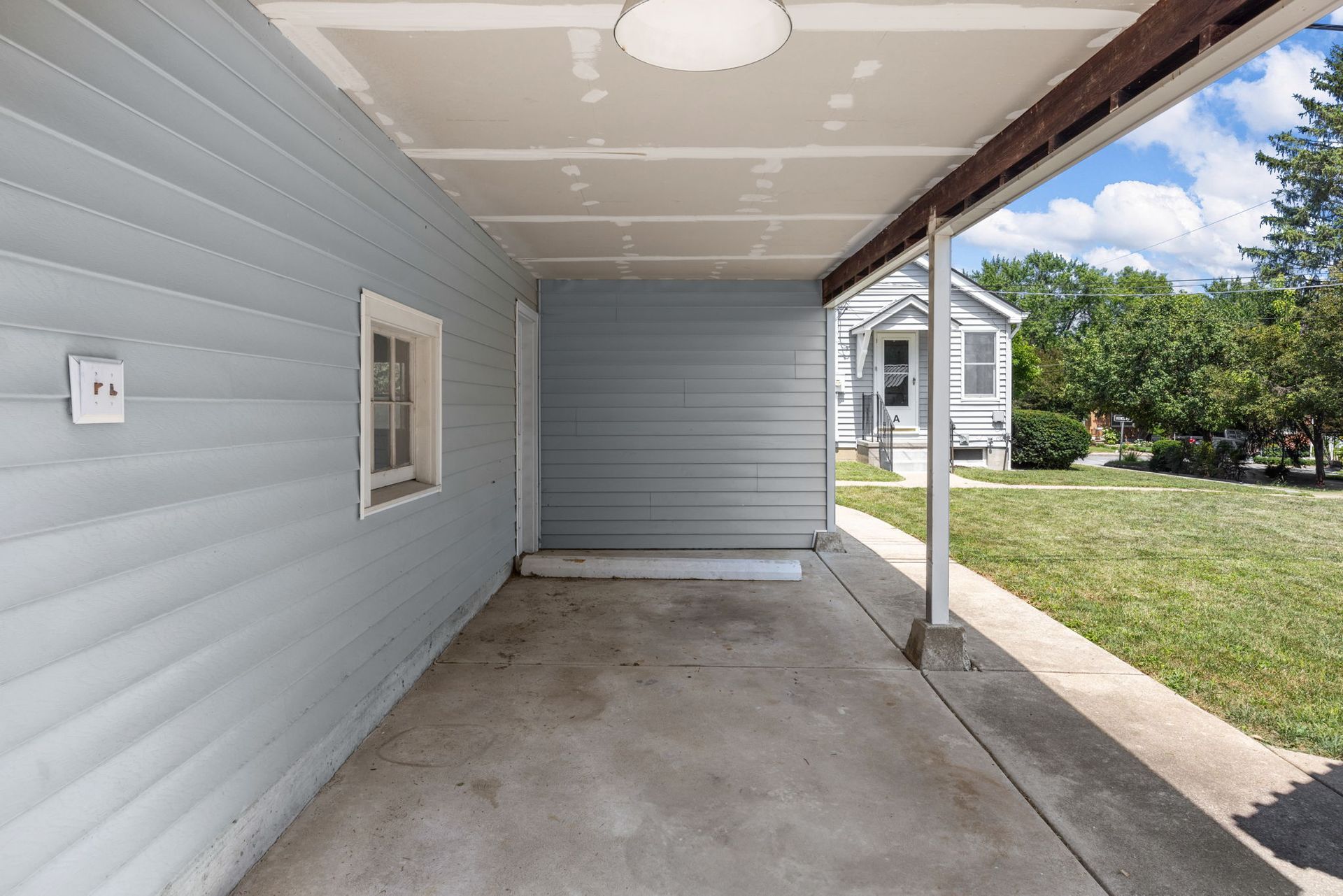 An empty driveway with a covered porch and a window on the side of a house.