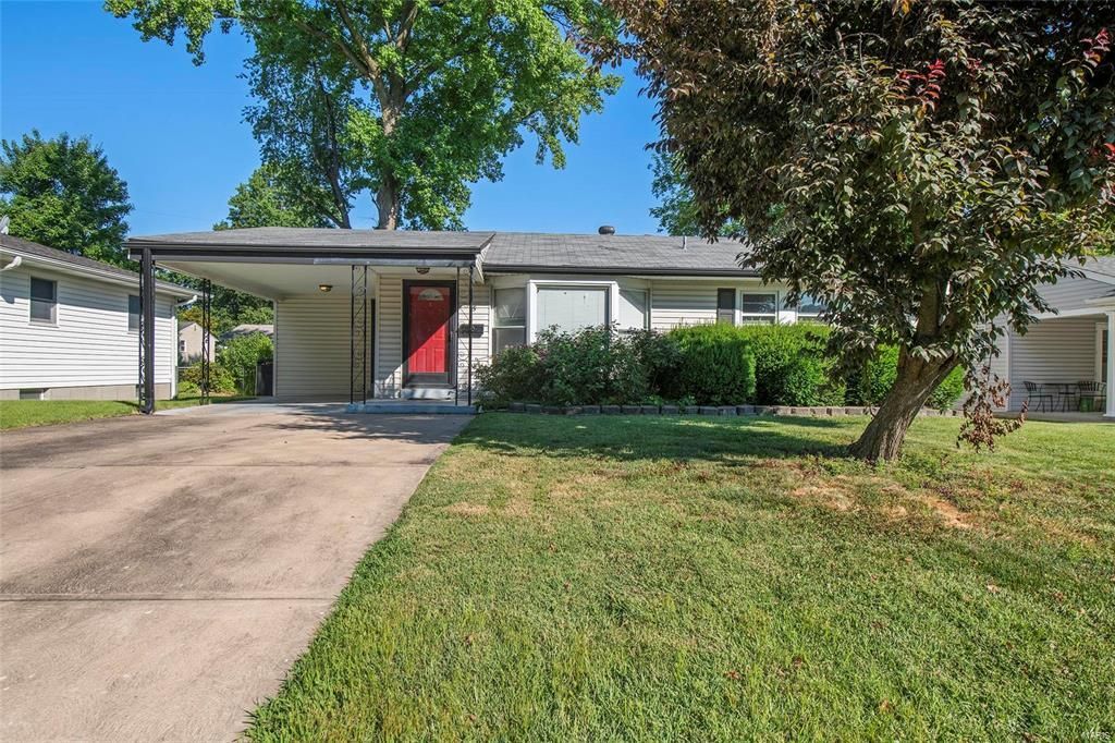 A white house with a red door and a tree in front of it.