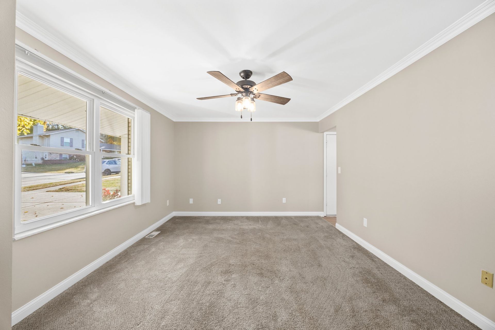 An empty living room with a ceiling fan and two windows.