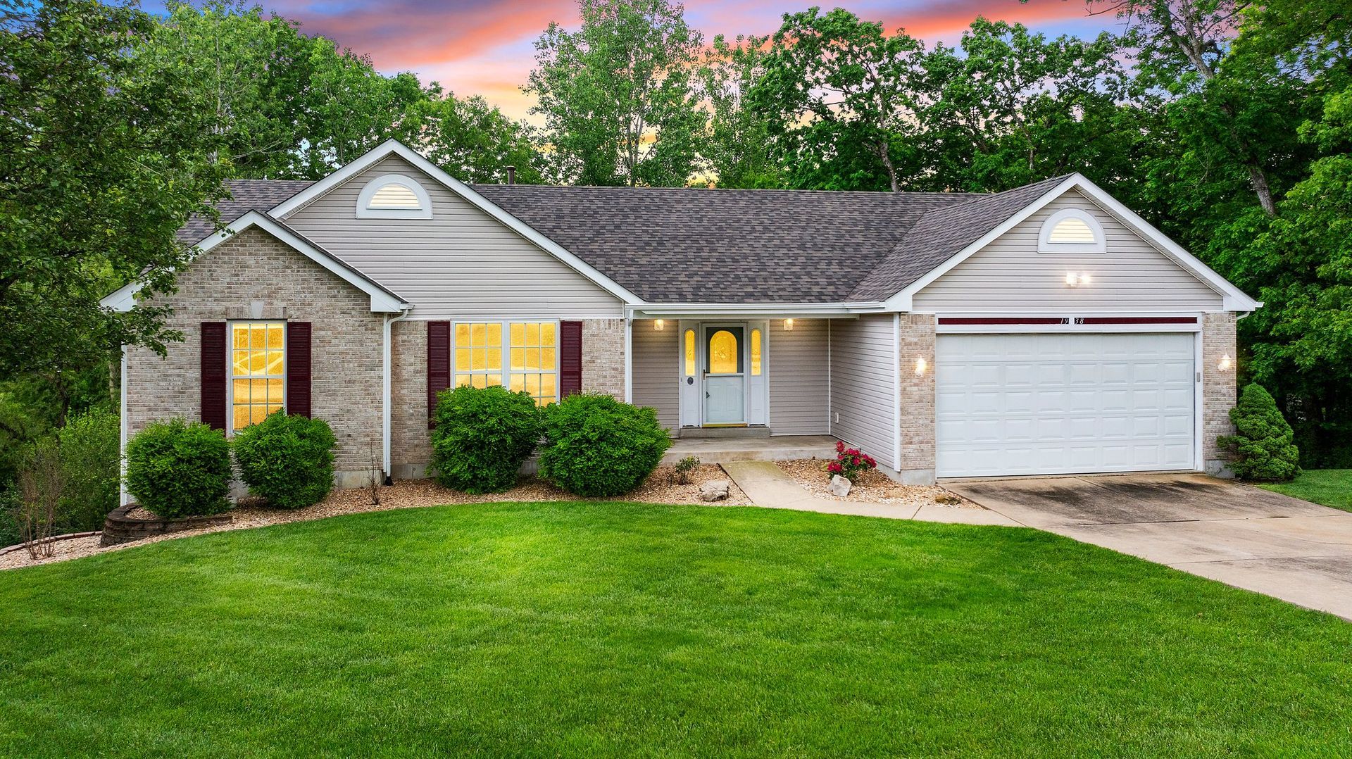 A brick house with a white garage door and a large lawn in front of it.