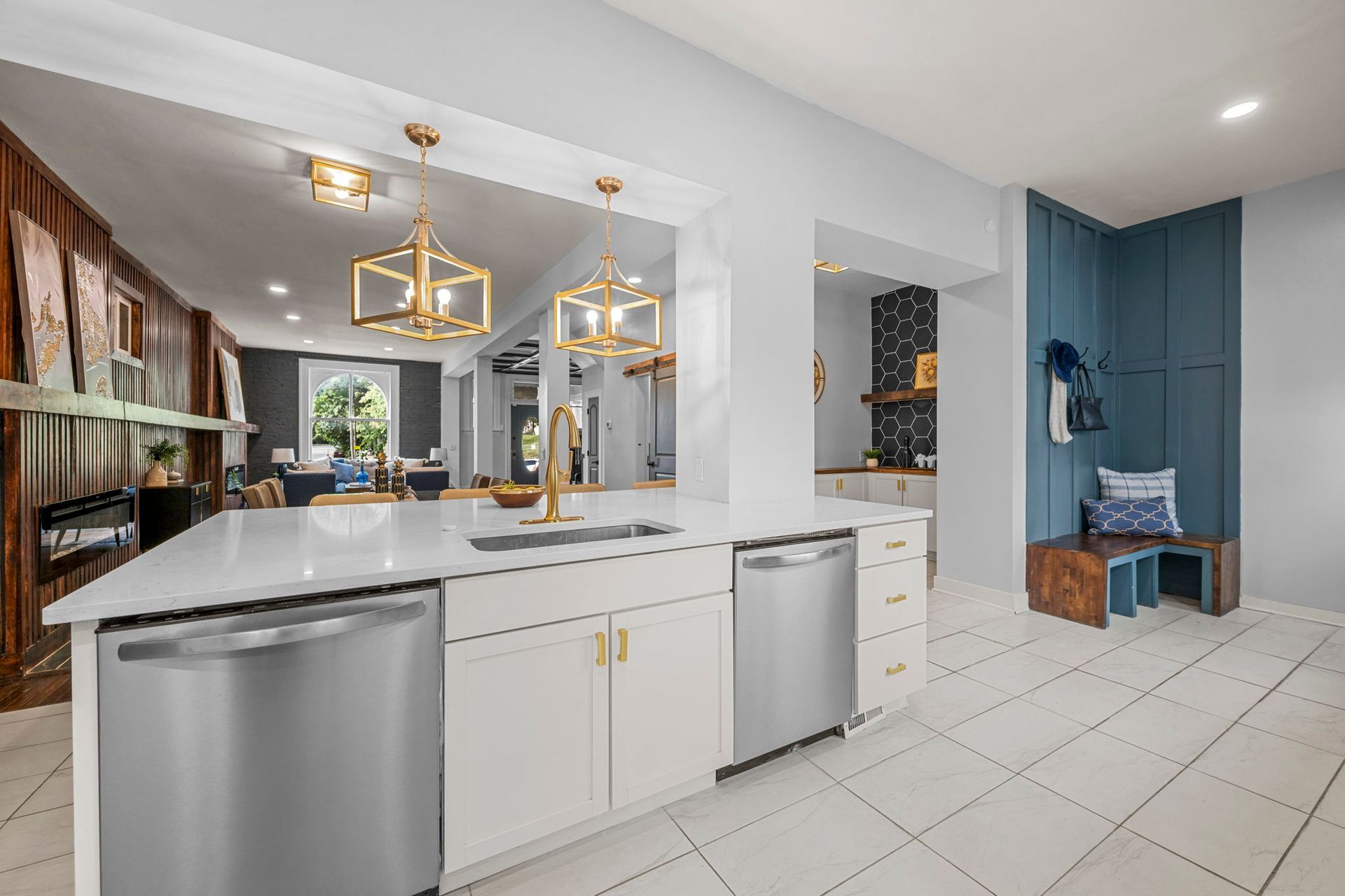 Modern kitchen with white island, gold fixtures, and open layout. Light blue accent wall with bench.