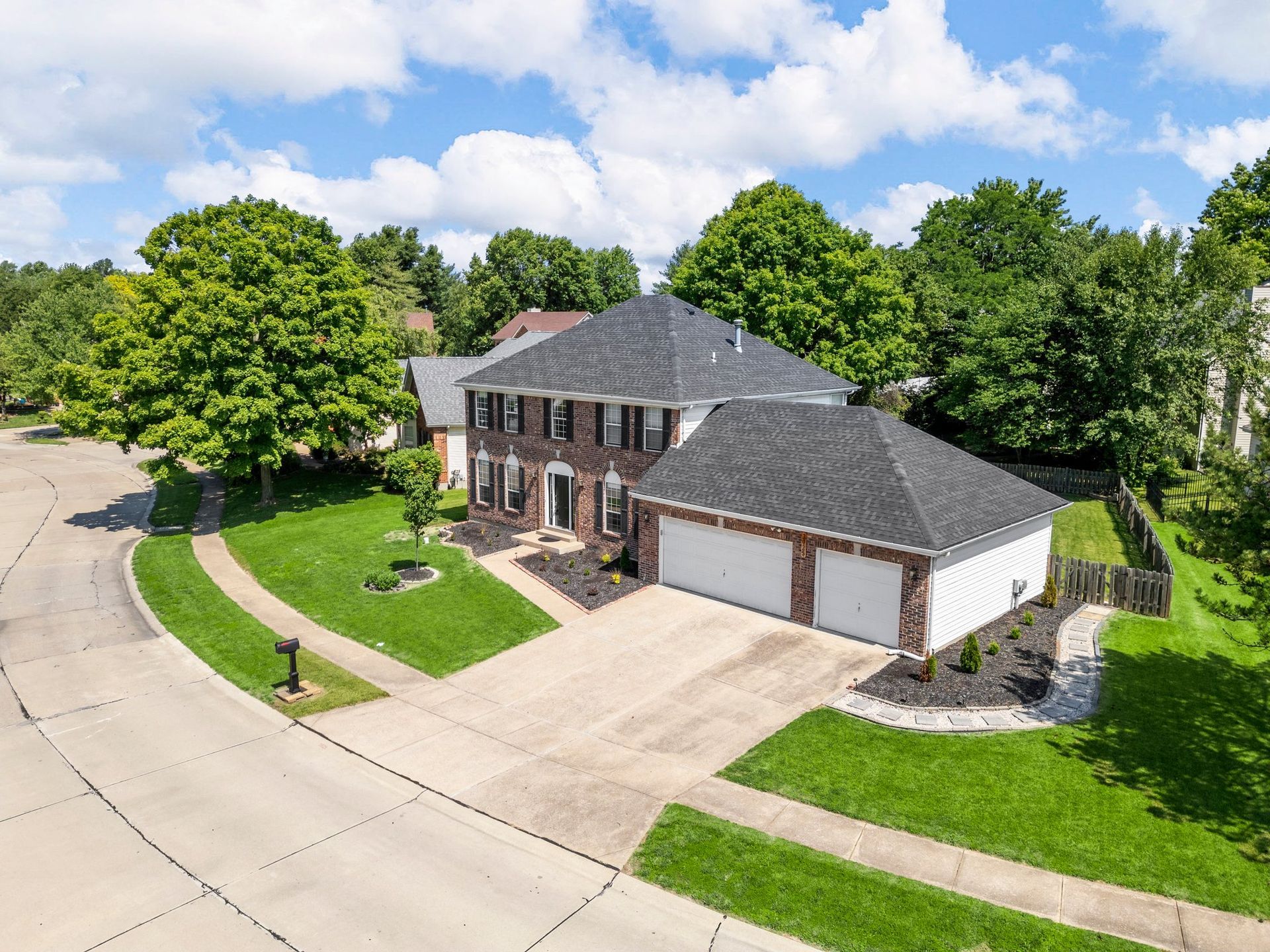 An aerial view of a house with a black roof and a large driveway.