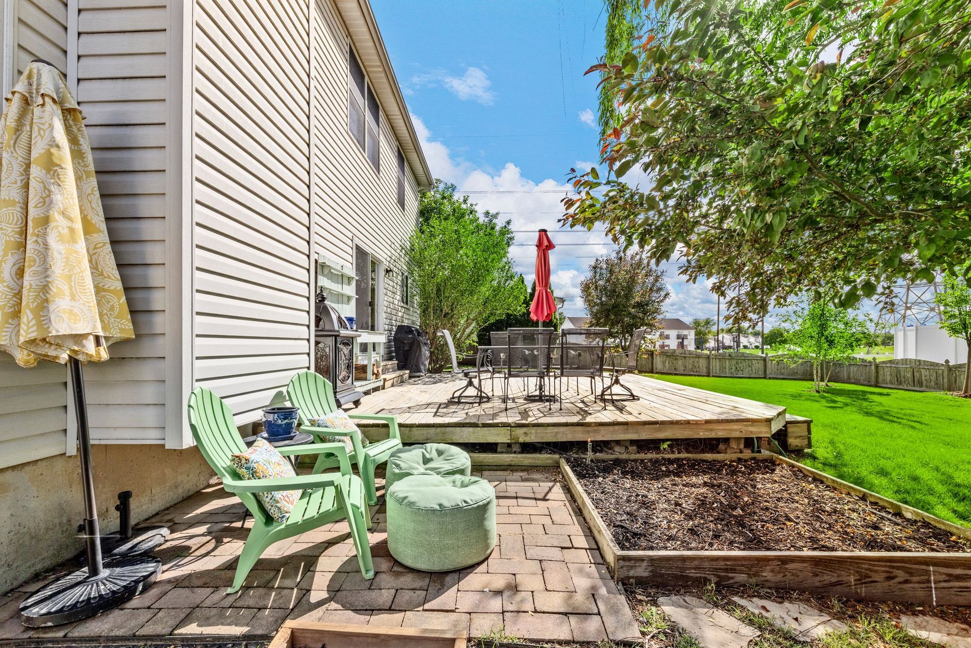A backyard with a deck , chairs , ottomans and a red umbrella.