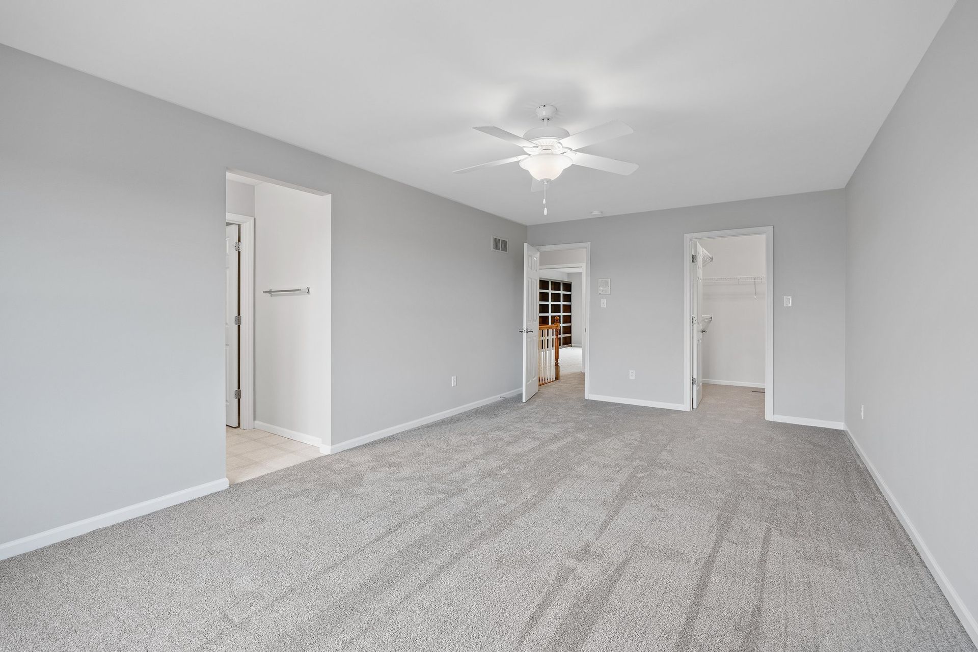 An empty living room with a ceiling fan and gray carpet.