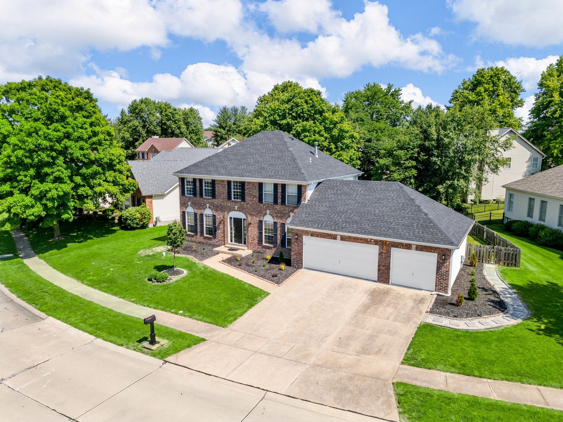 An aerial view of a large brick house with a large driveway surrounded by trees.