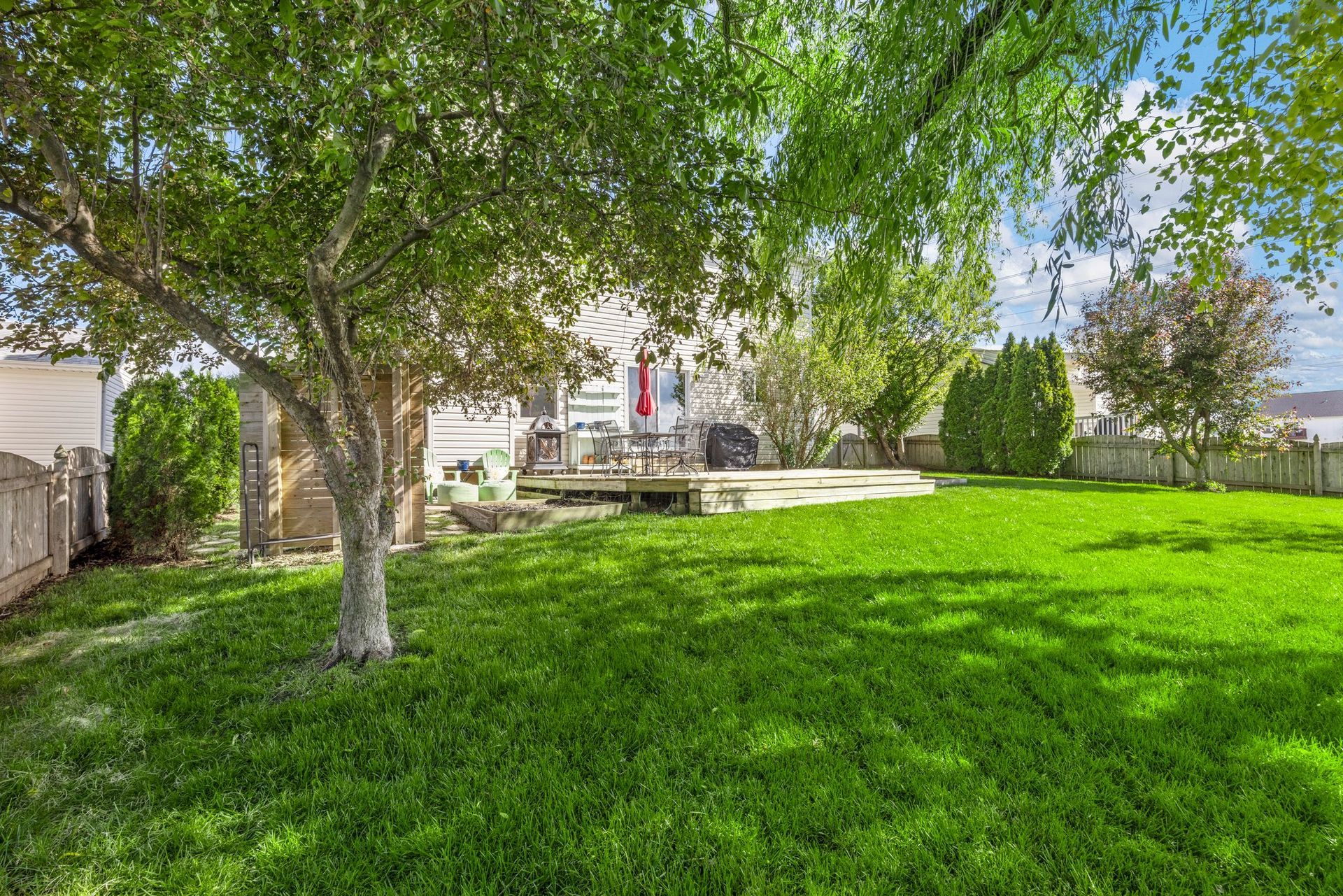 The backyard of a house with a large lush green lawn and trees.