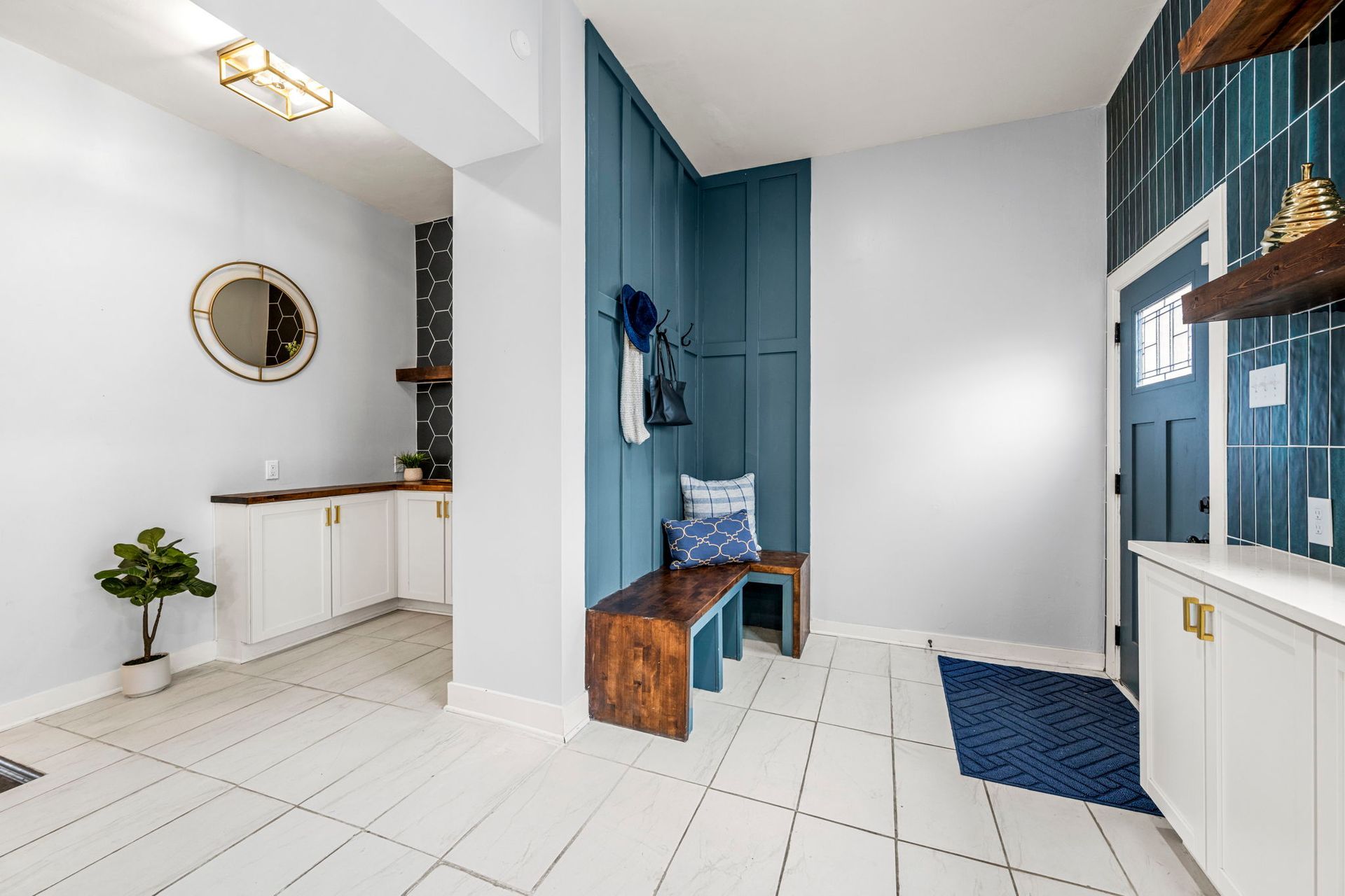 Modern entryway with white tile, blue accent wall with bench, and built-in white cabinets.