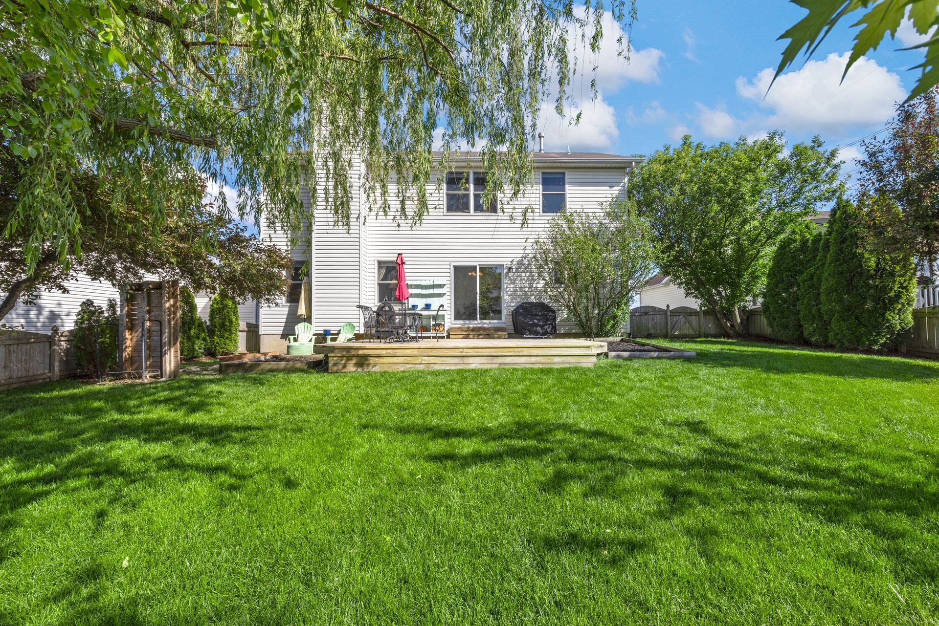 The backyard of a house with a large lush green lawn and a deck.