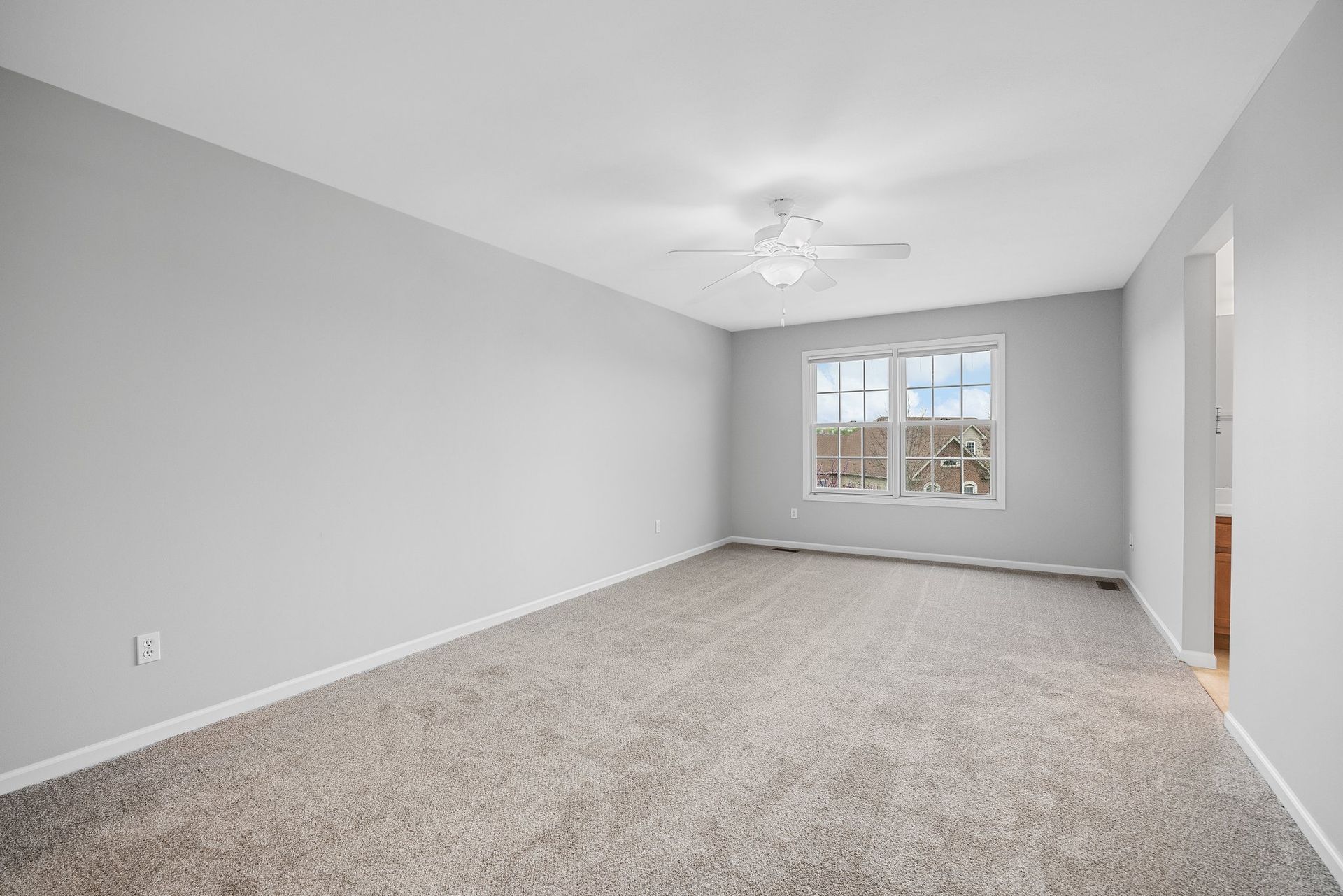 An empty living room with a ceiling fan and two windows.