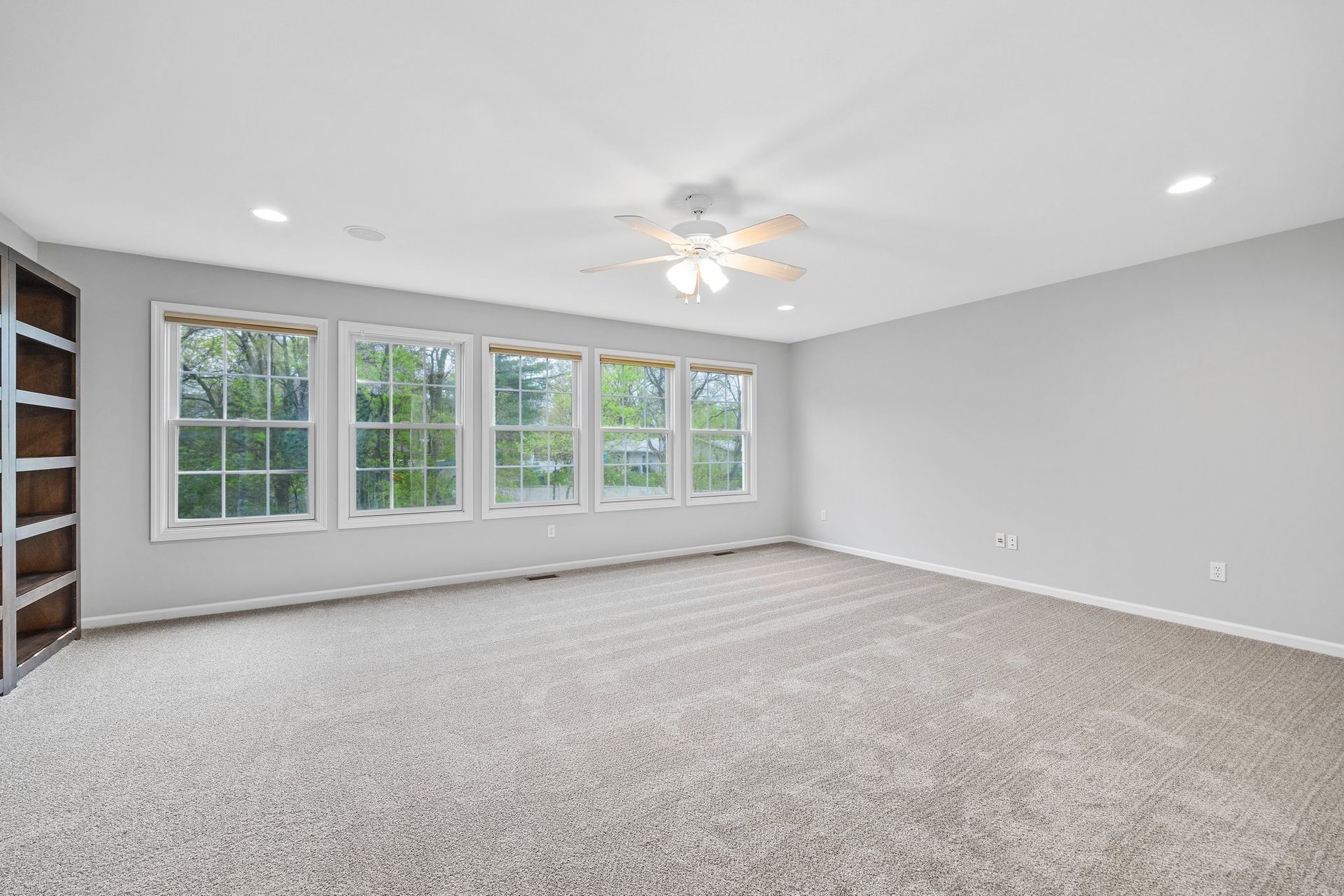 A large empty room with a lot of windows and a ceiling fan.
