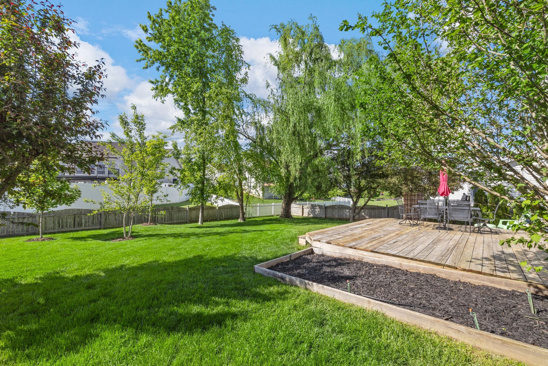 A large lush green yard with trees and a wooden deck.