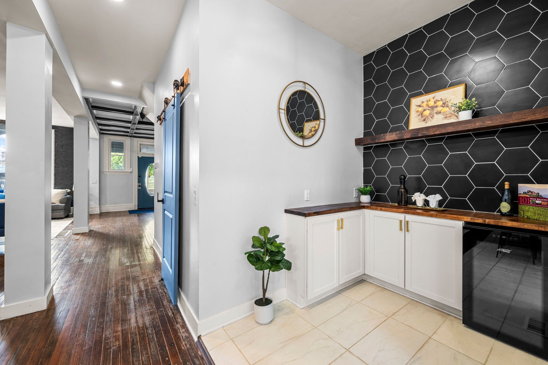 A hallway with a home bar featuring black hexagon tile and white cabinets.