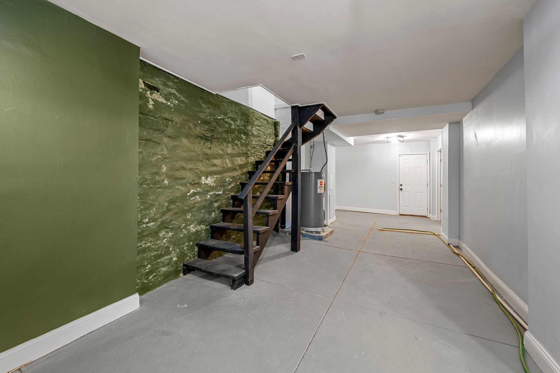 Basement with dark wooden stairs, green and gray walls, and concrete floor.