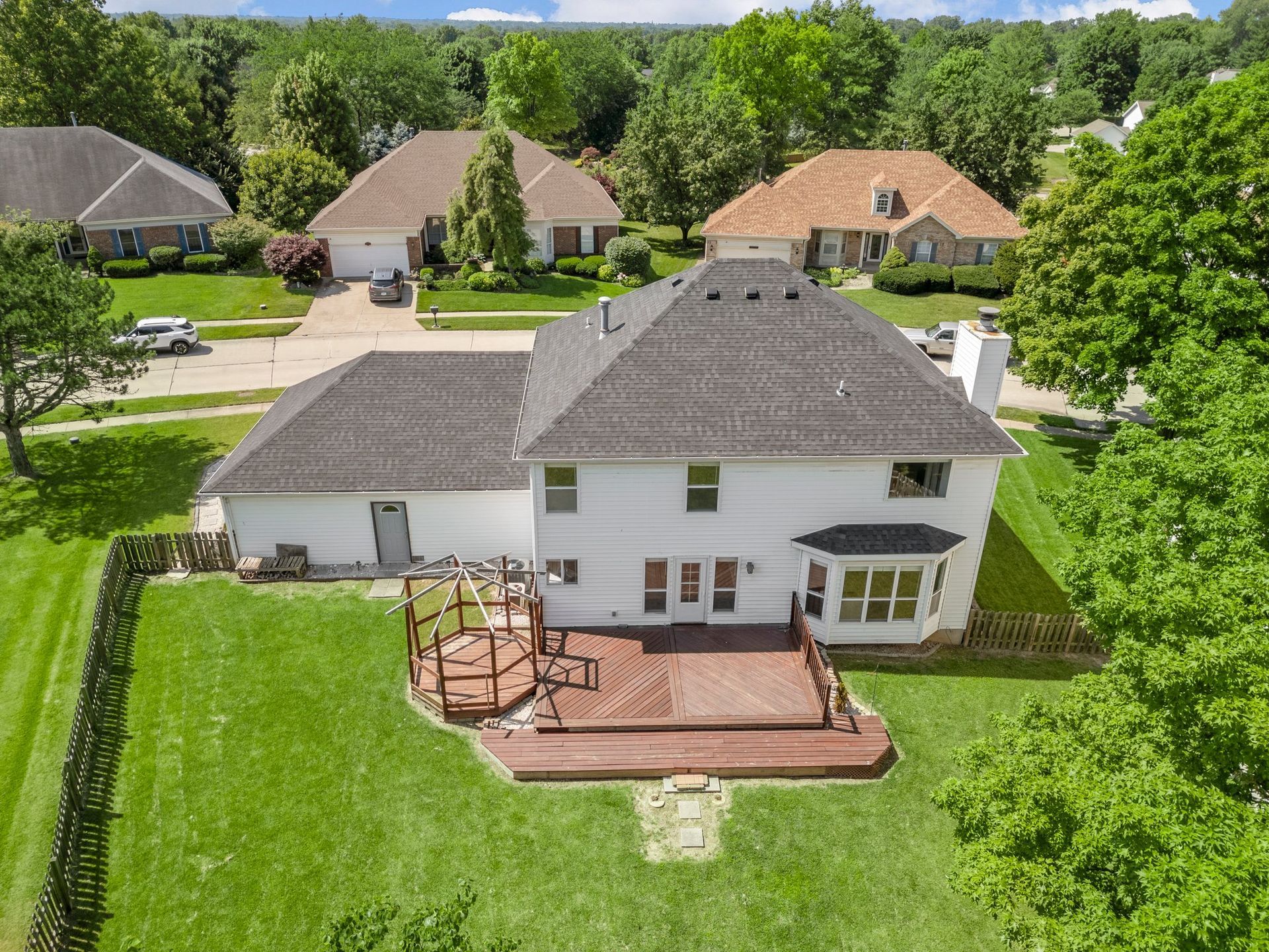 An aerial view of a large white house with a brick deck surrounded by trees.
