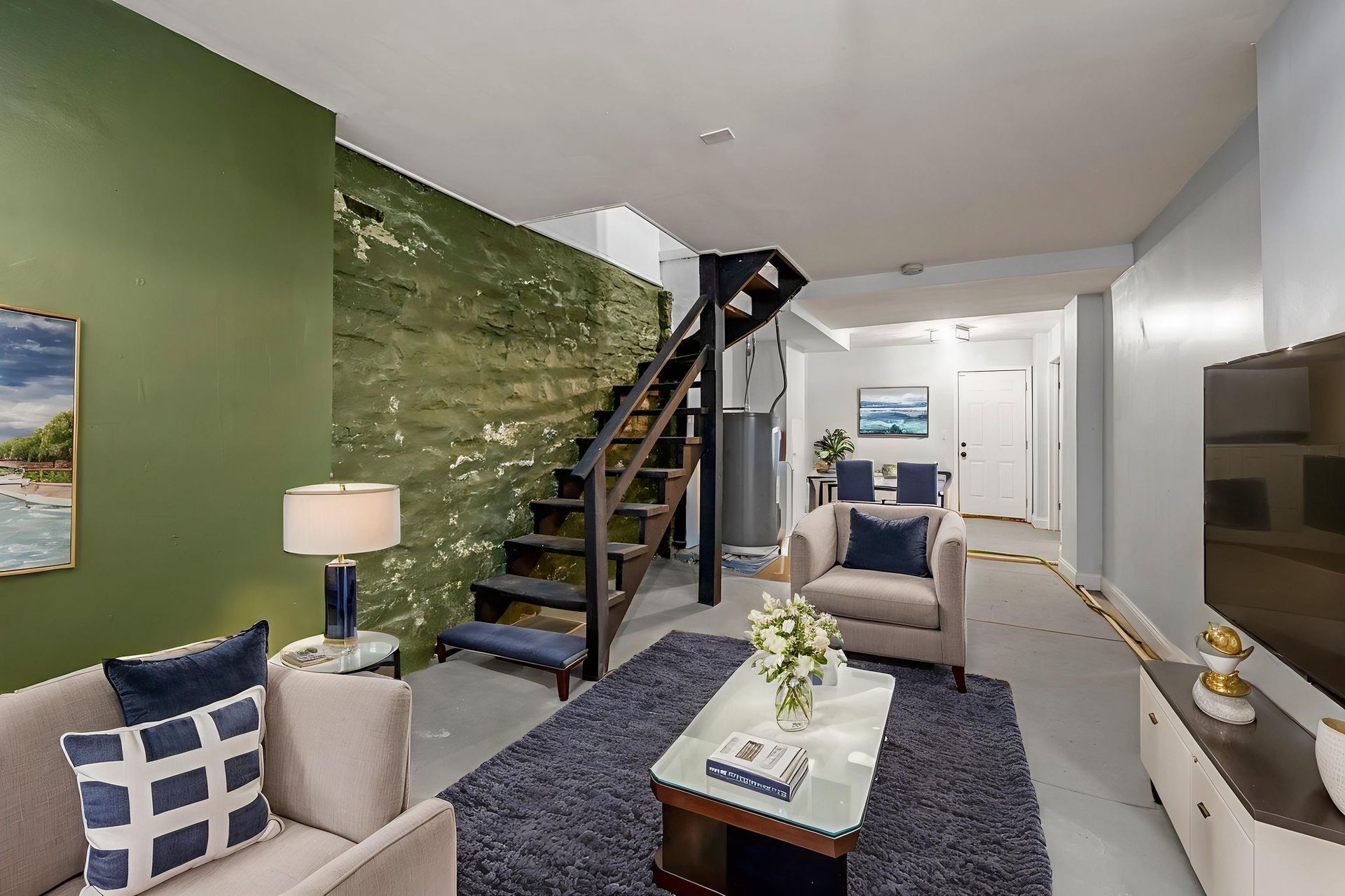 Living room with stairs, green wall, sofa, rug, and TV.
