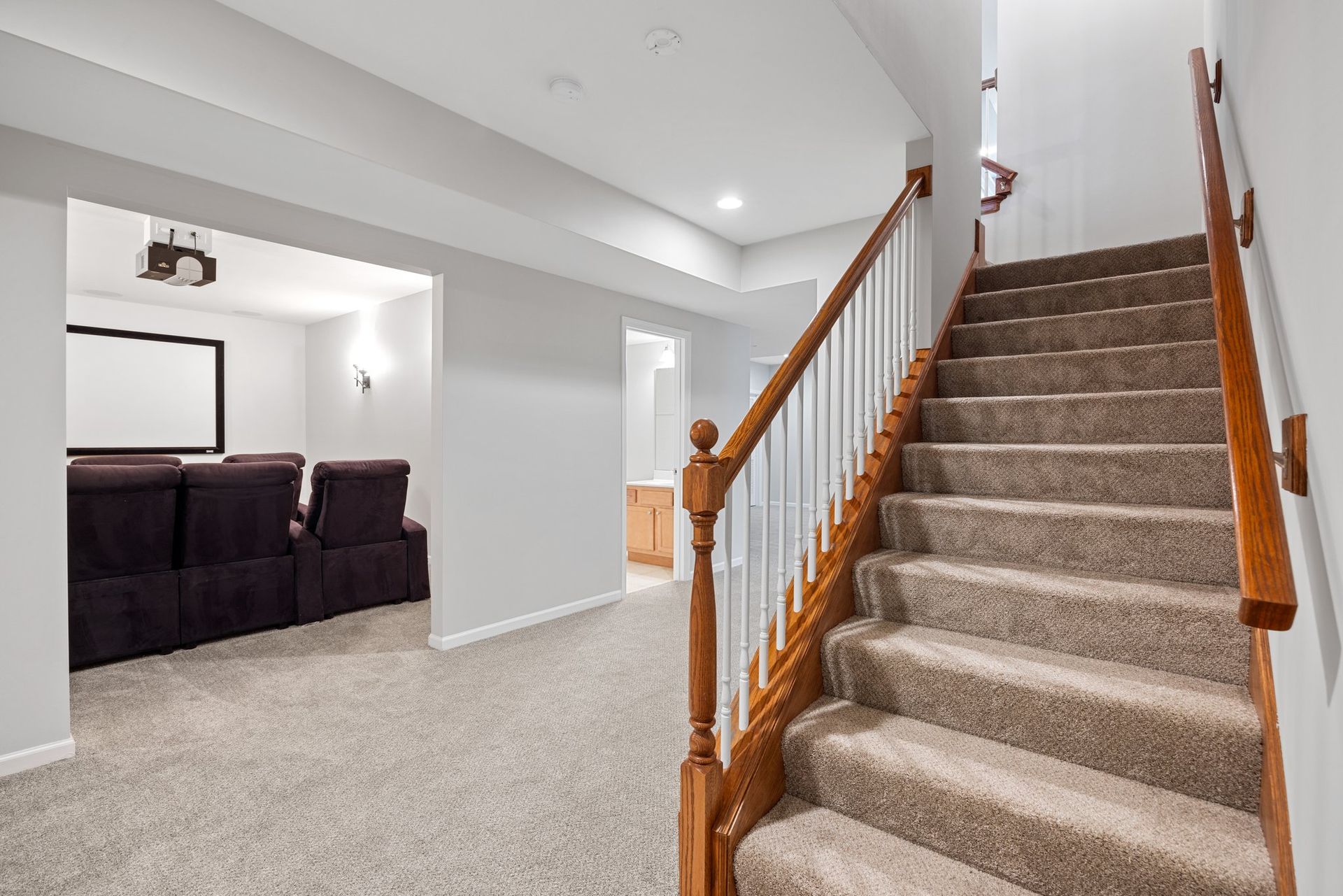 A basement with carpeted floors and stairs leading up to the second floor.