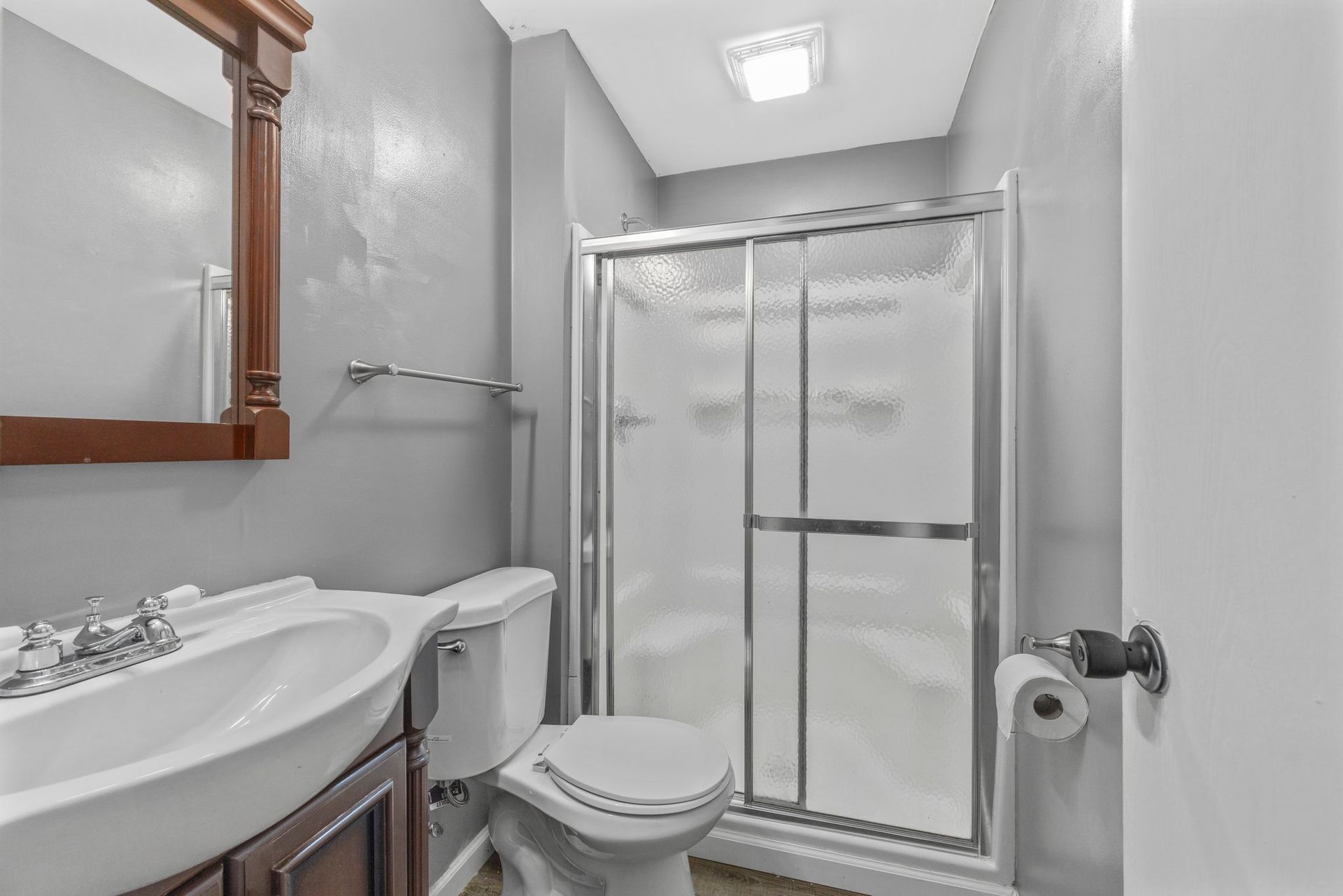 A bathroom with a toilet , sink , mirror and shower stall.