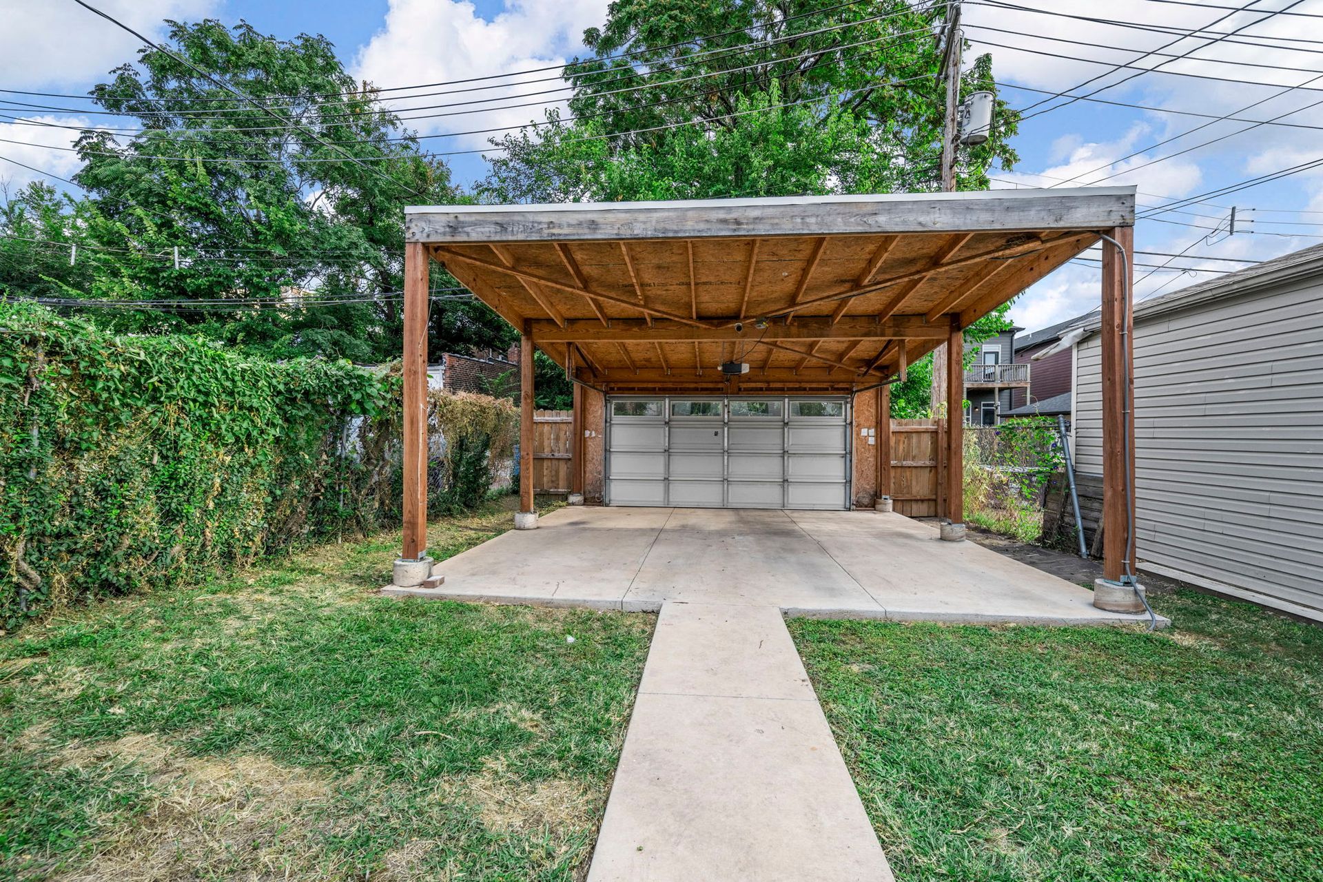 Backyard with carport, garage, concrete pathway, and green lawn.