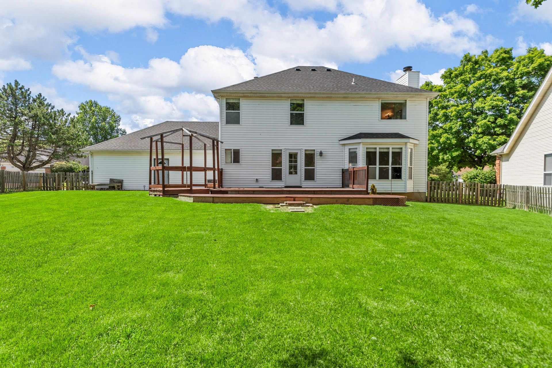 The backyard of a house with a large lawn and a deck.