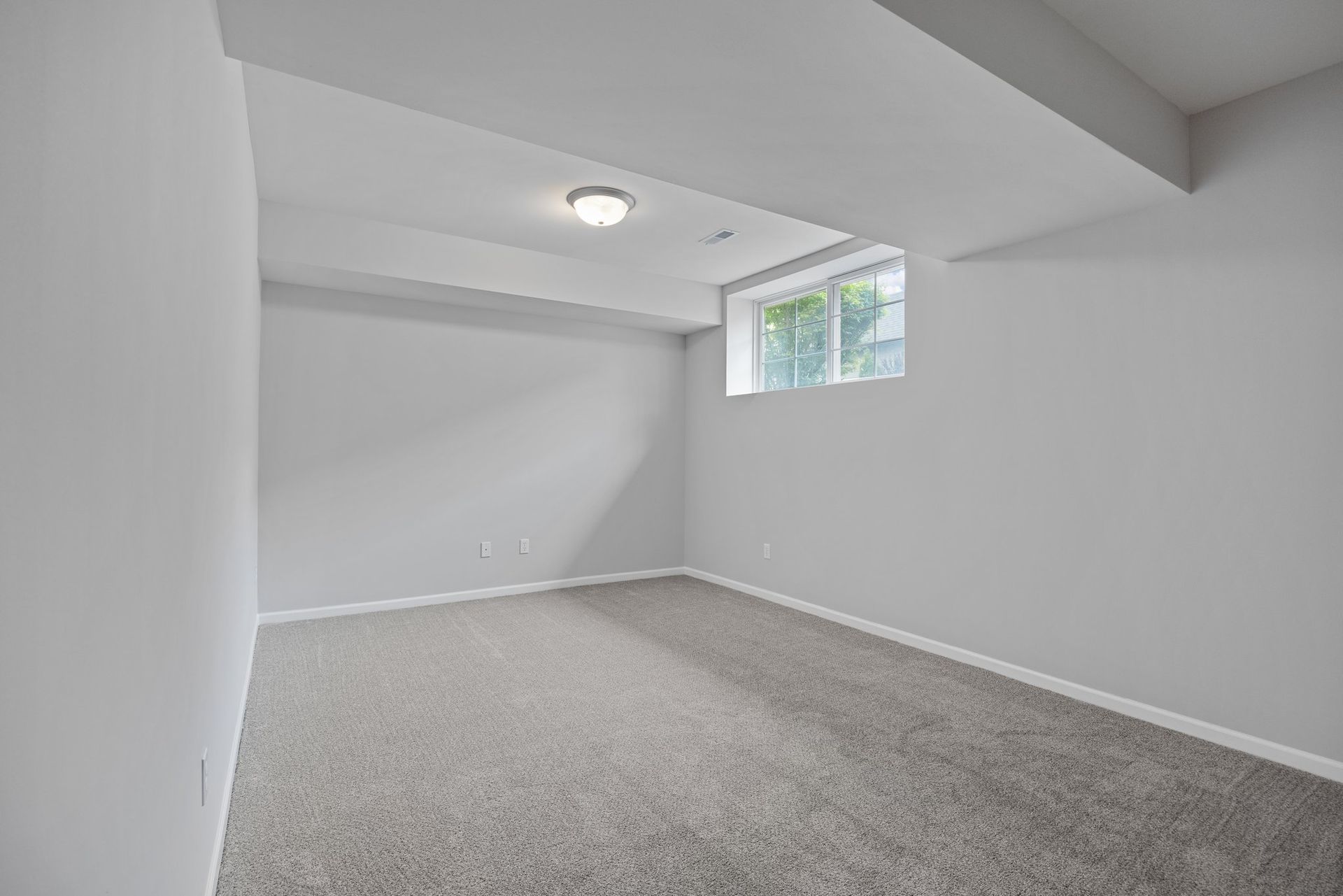 An empty basement with a window and carpet.