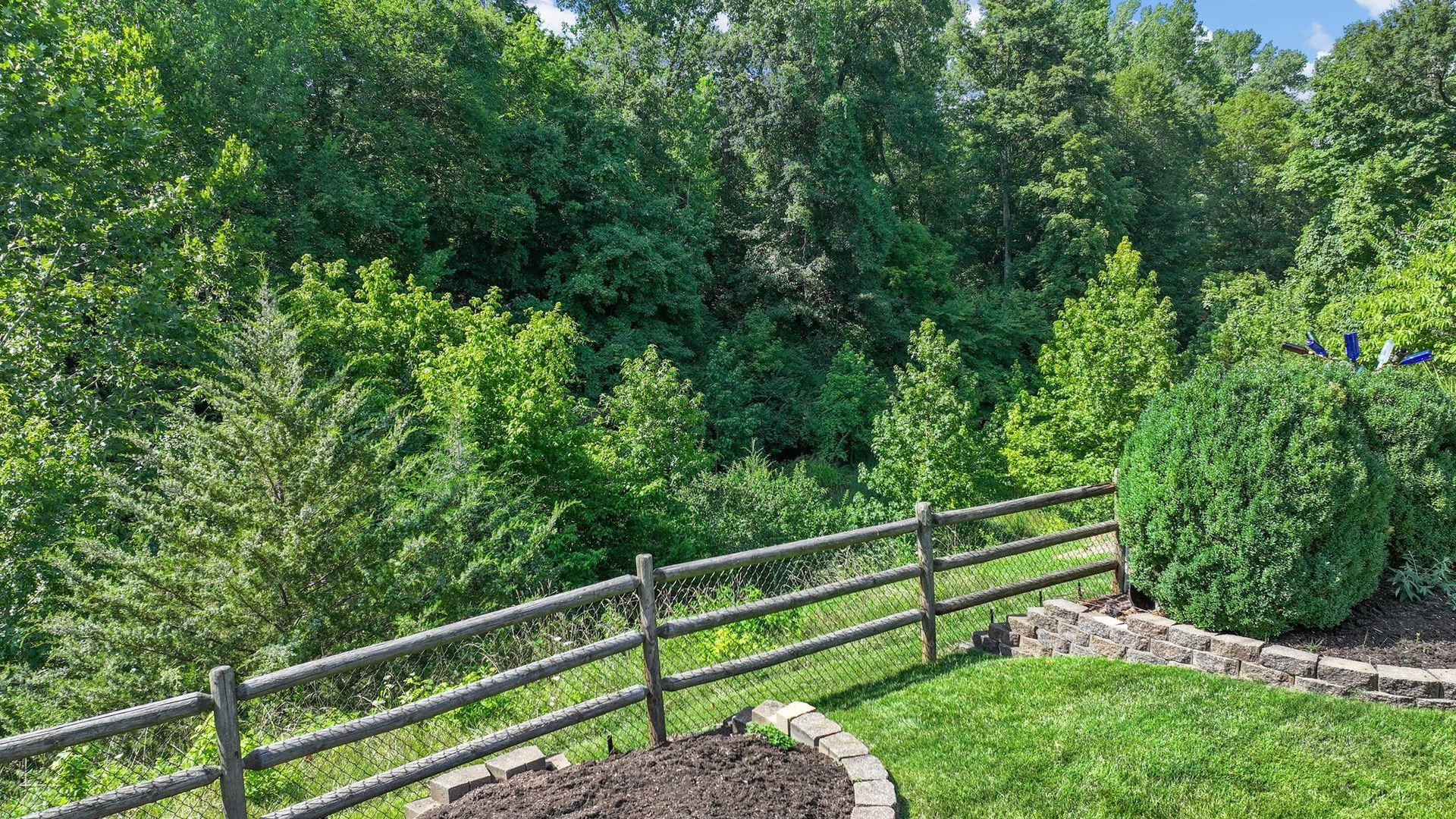 A wooden fence surrounds a lush green field with trees in the background.