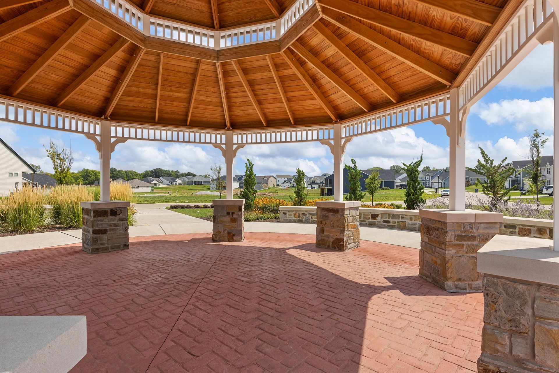 A gazebo with a wooden roof and brick floor in a park.