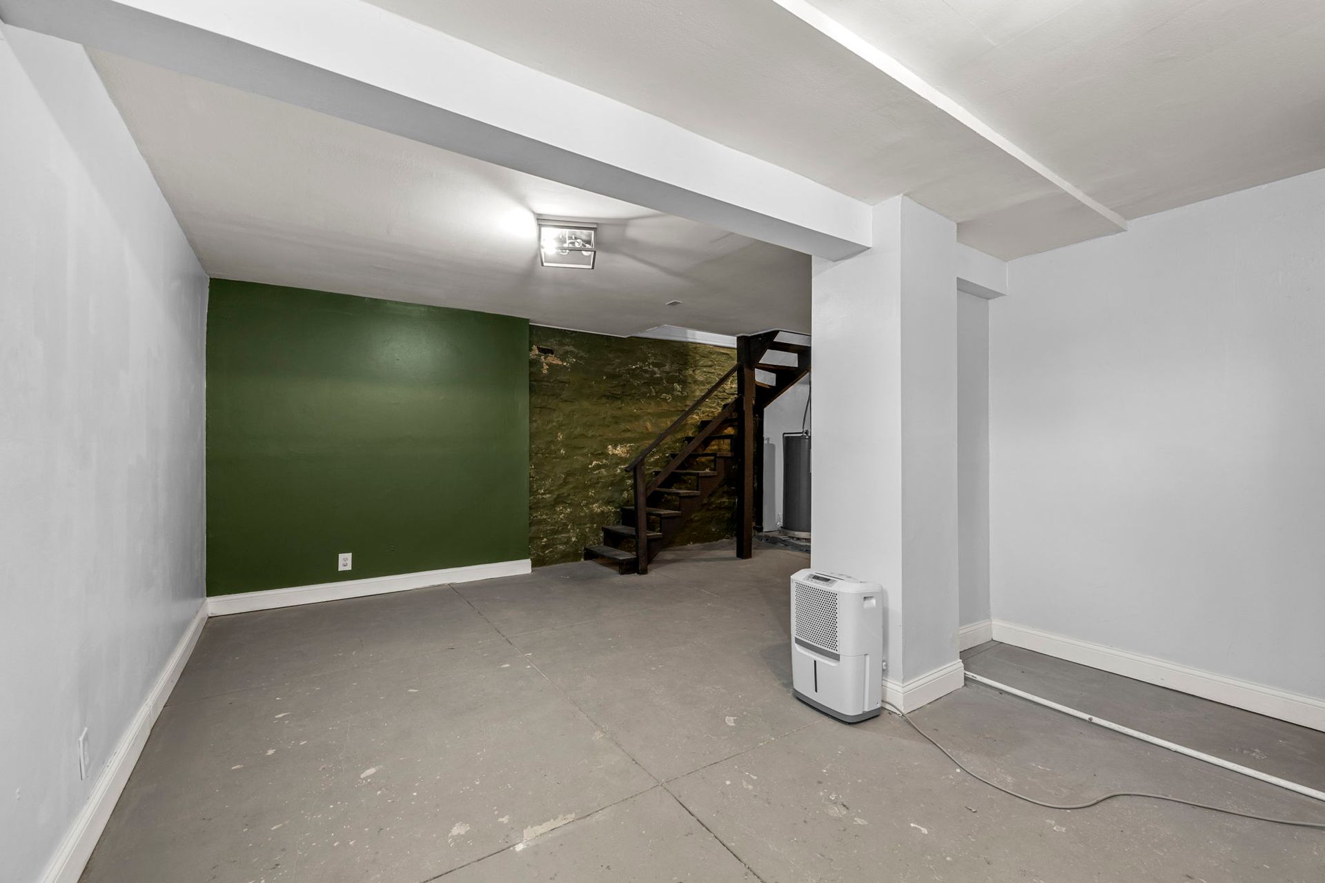 Empty room with green accent wall, stairs, dehumidifier, and exposed brick.