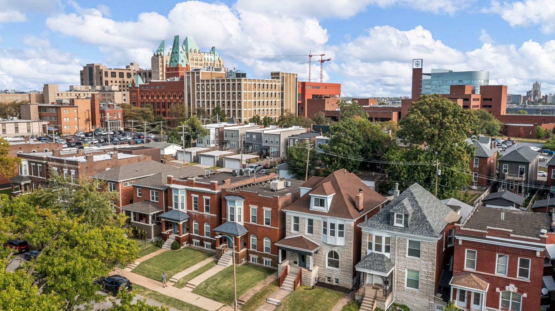 Cityscape with row houses in foreground, tall buildings in background under a blue sky.