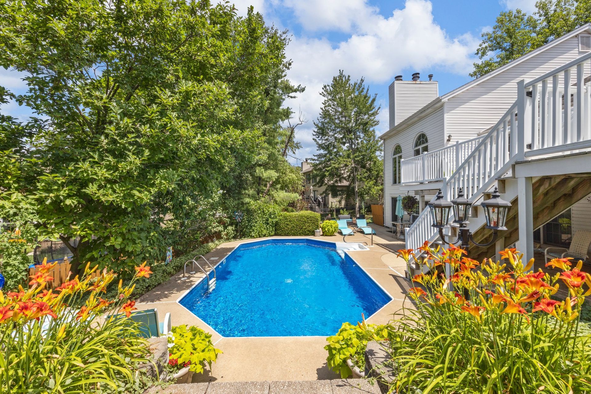 A large swimming pool in the backyard of a house surrounded by trees and flowers.