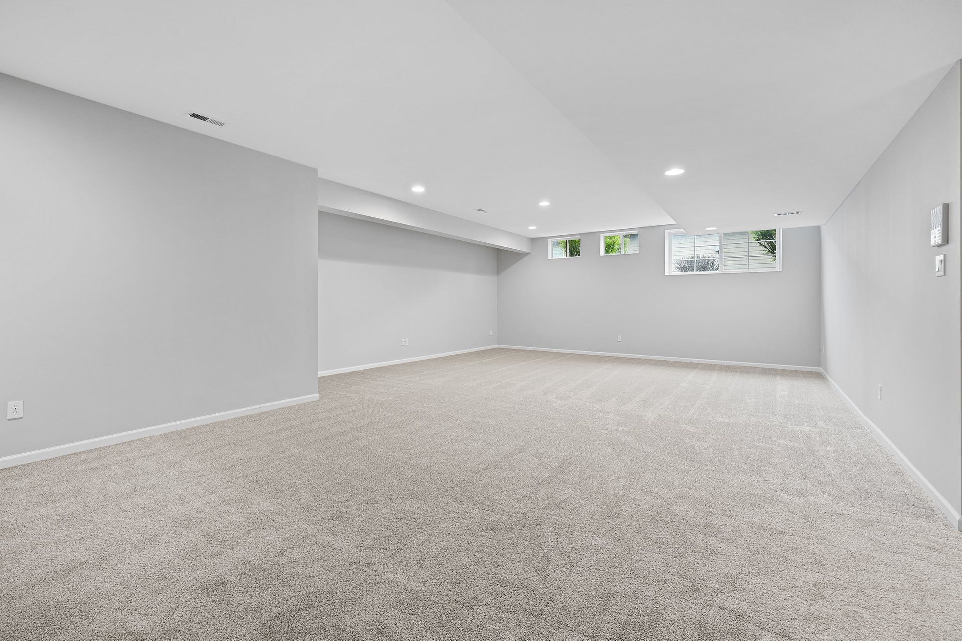 An empty basement with a carpeted floor and white walls.